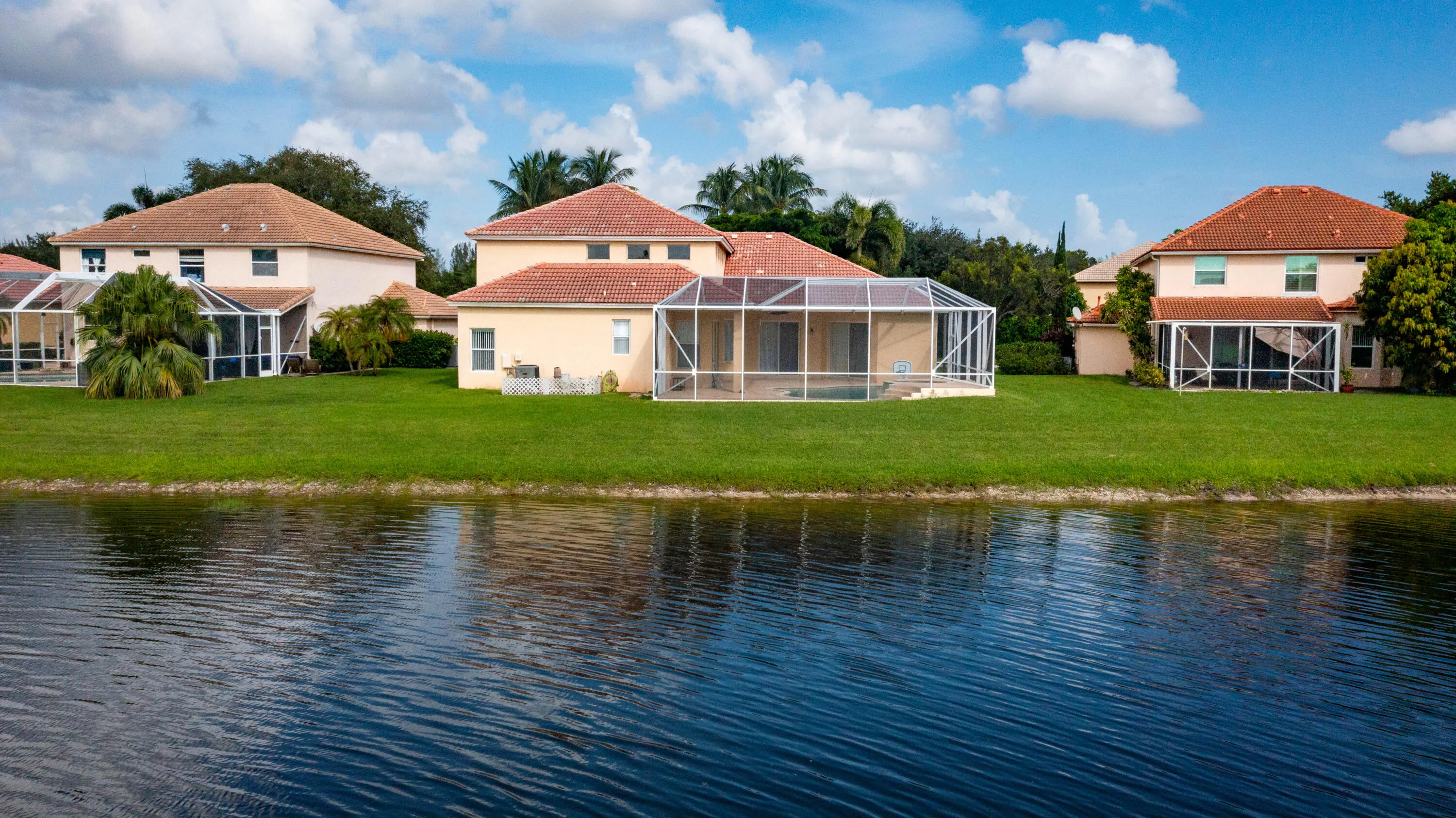 Lakeside property featuring a screened-in pool enclosure, large lawn, and mature landscaping