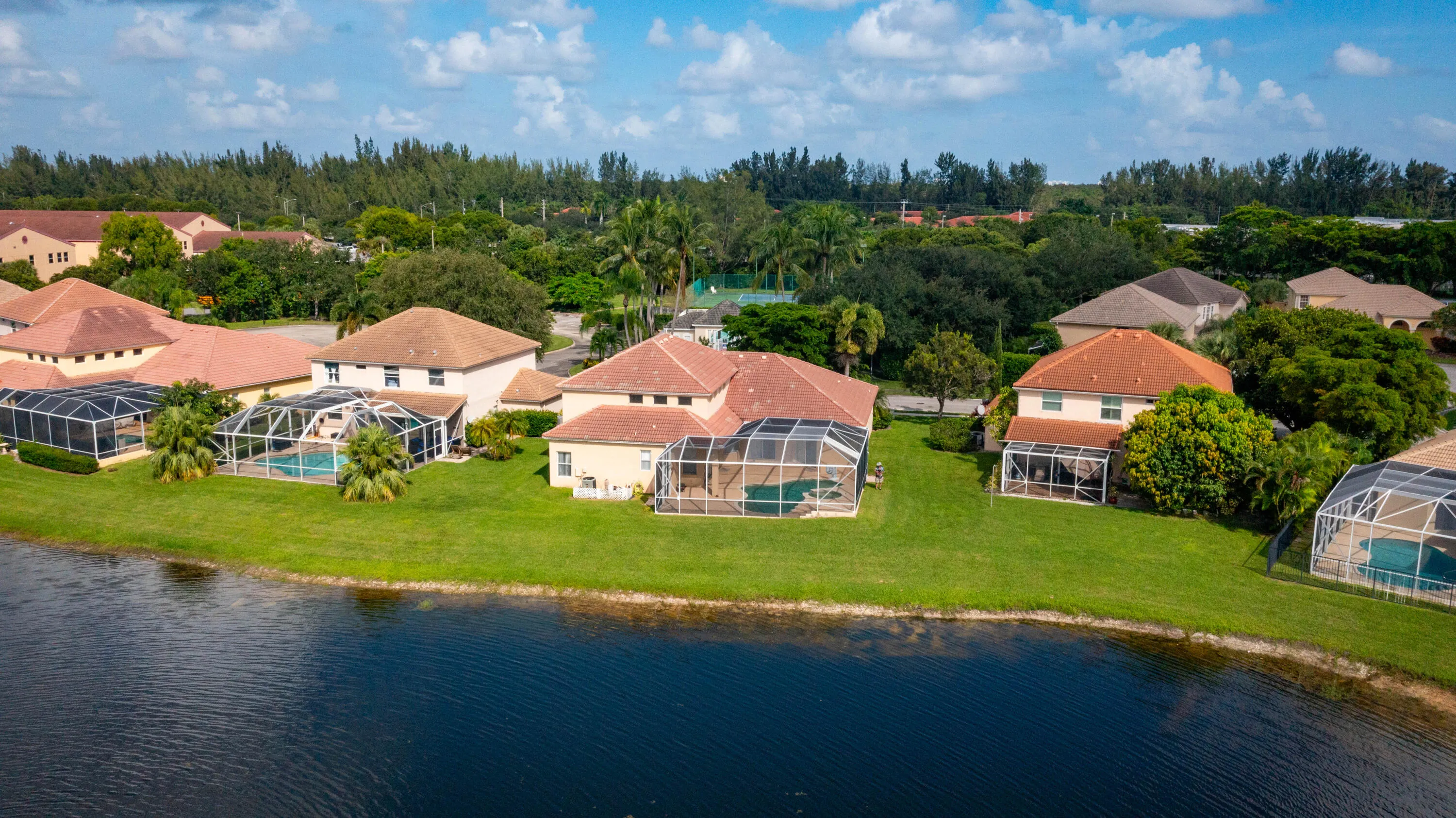 Waterfront property featuring a screened-in pool enclosure, mature landscaping, and a red tile roof