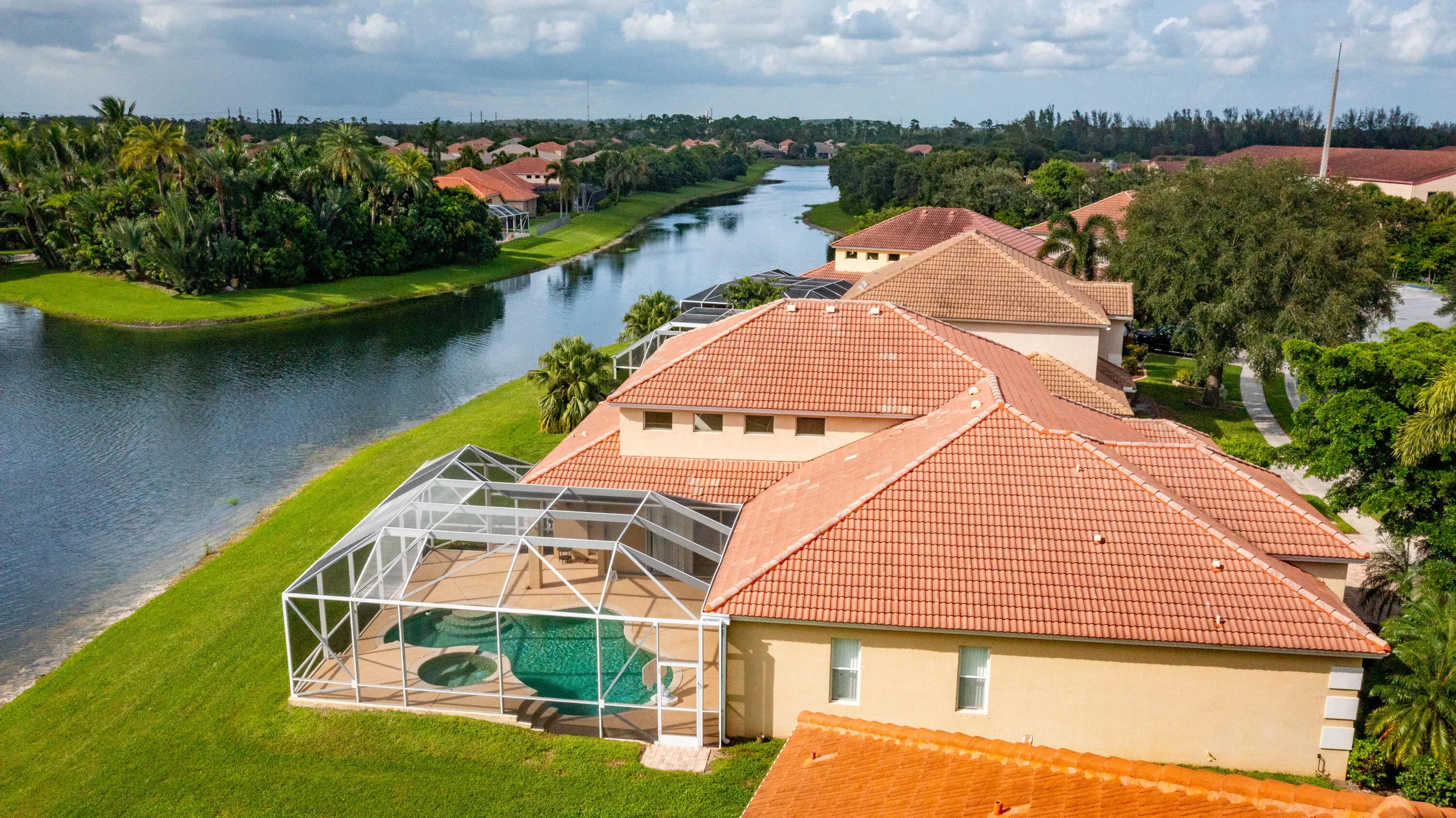 Waterfront property featuring a screened-in pool and spa, terracotta tile roofing, and a manicured lawn