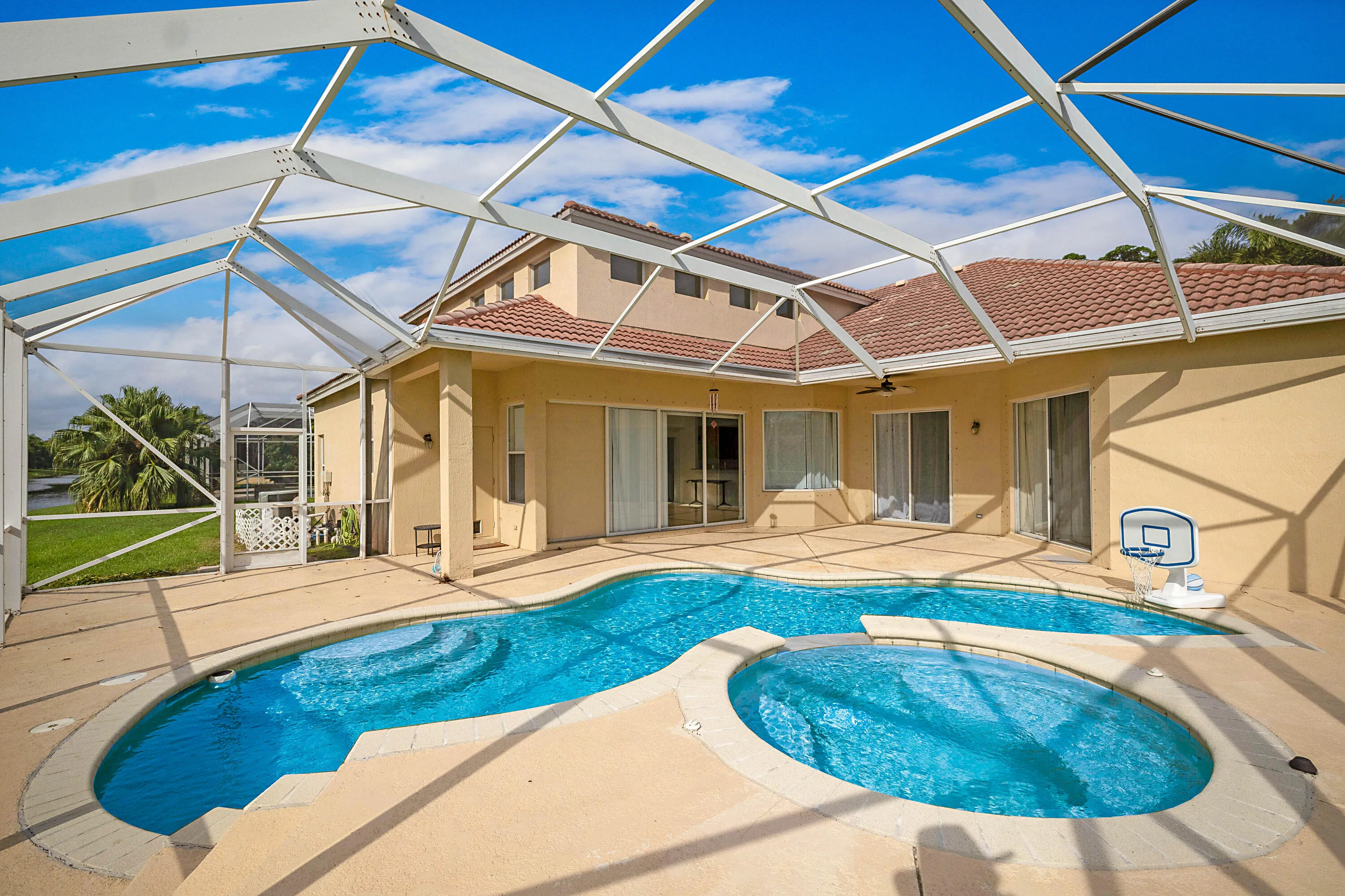 Screened lanai with retractable shade system overlooking resort-style pool featuring dual kidney-shaped sections with surrounding decking