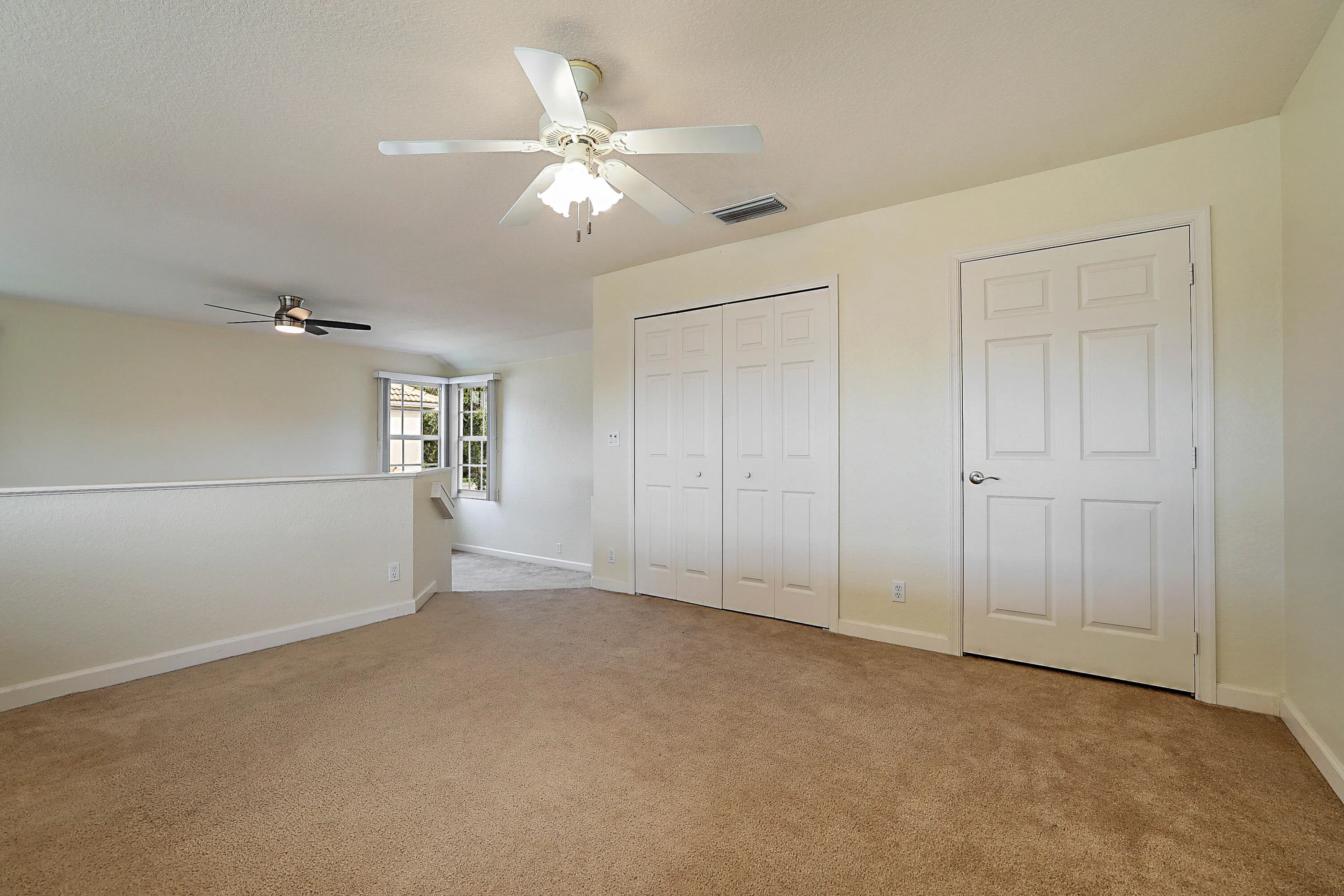 Spacious bedroom featuring neutral wall finishes, wall-to-wall carpeting, dual closets with six-panel doors, and ceiling fan with integrated lighting