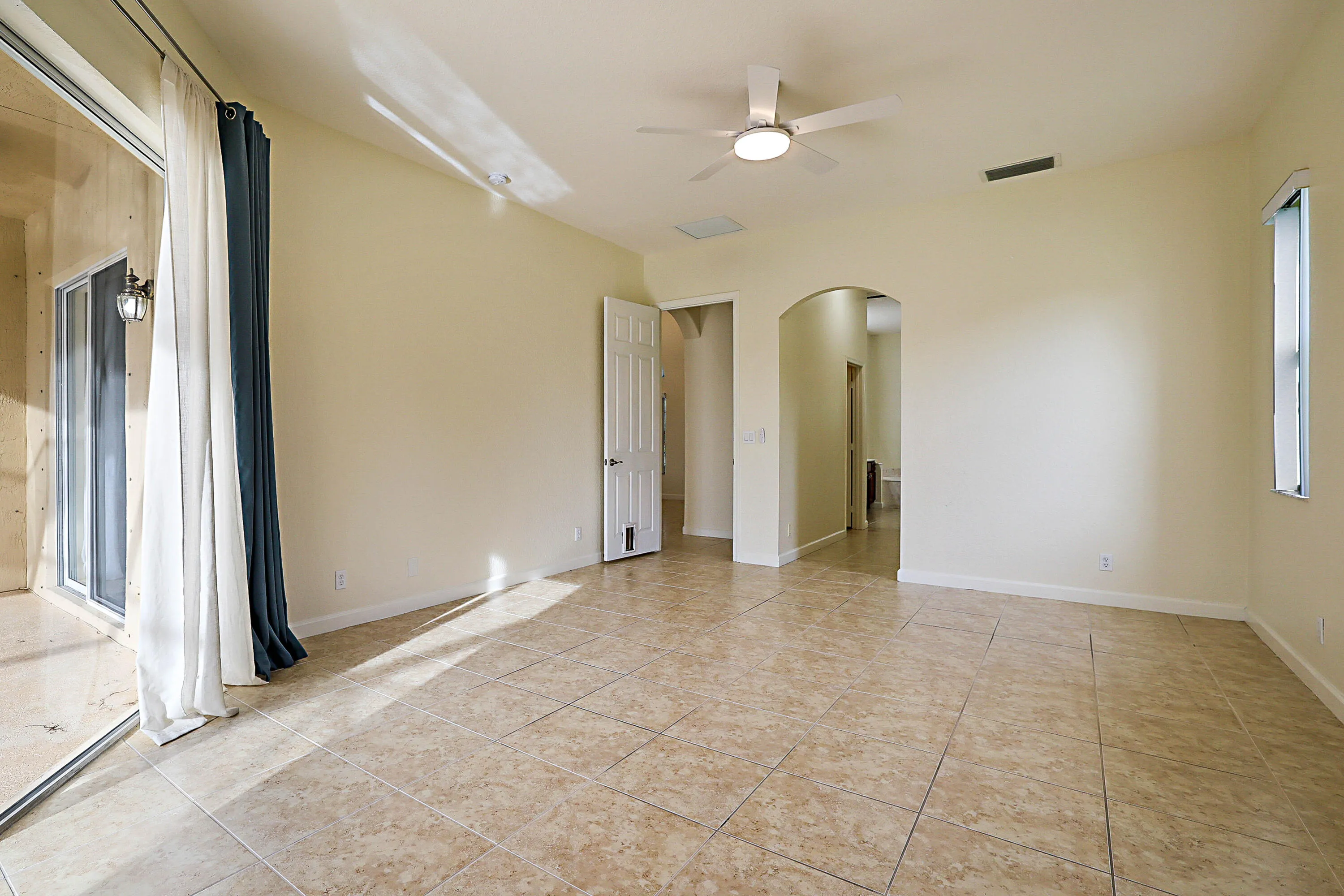 Tile flooring, ceiling fan with integrated lighting, arched doorway, sliding glass door, and a single vertical window