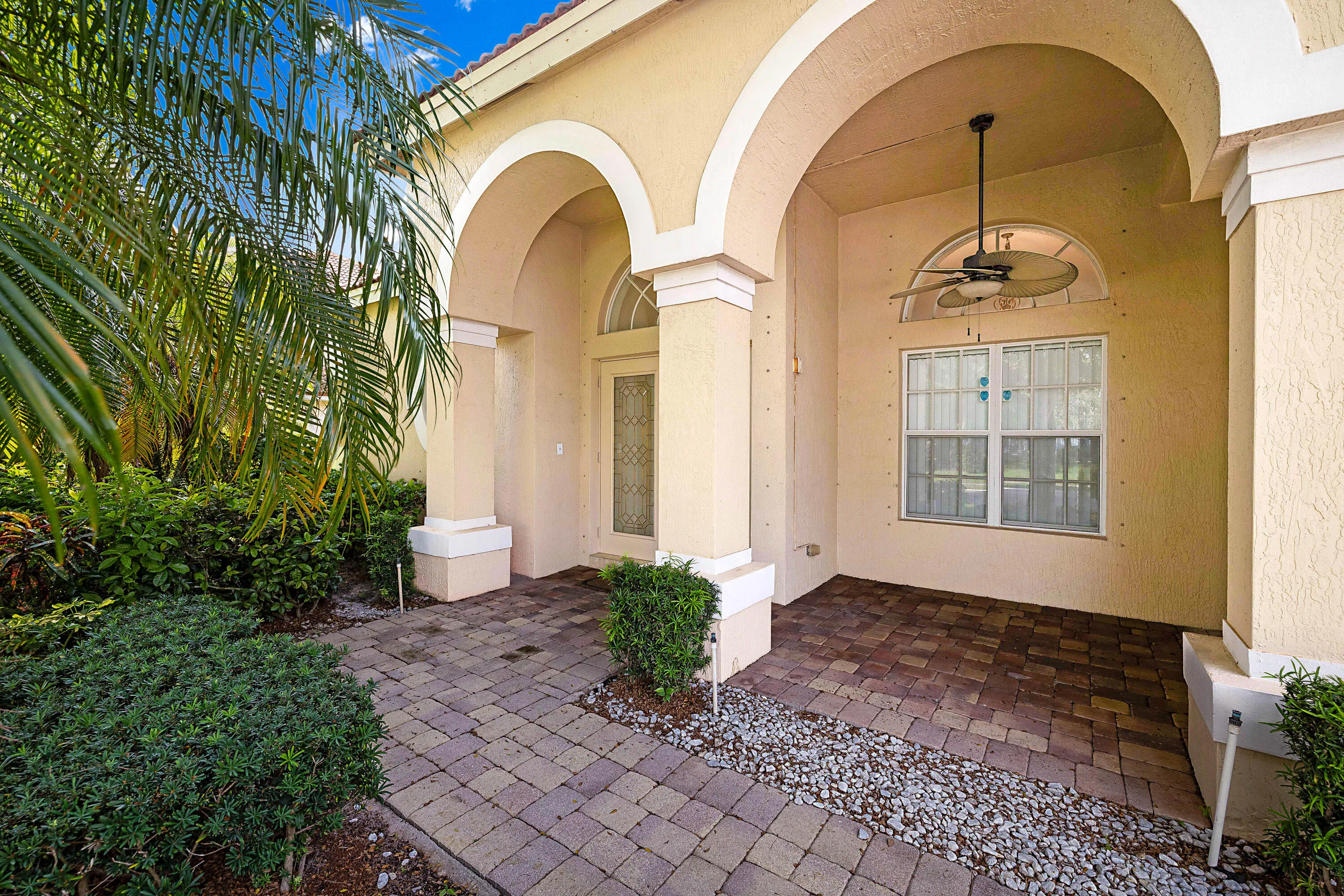 Front entry featuring arched architectural details, a covered patio area with a ceiling fan, a decorative glass entry door with an arched transom, and paver hardscaping