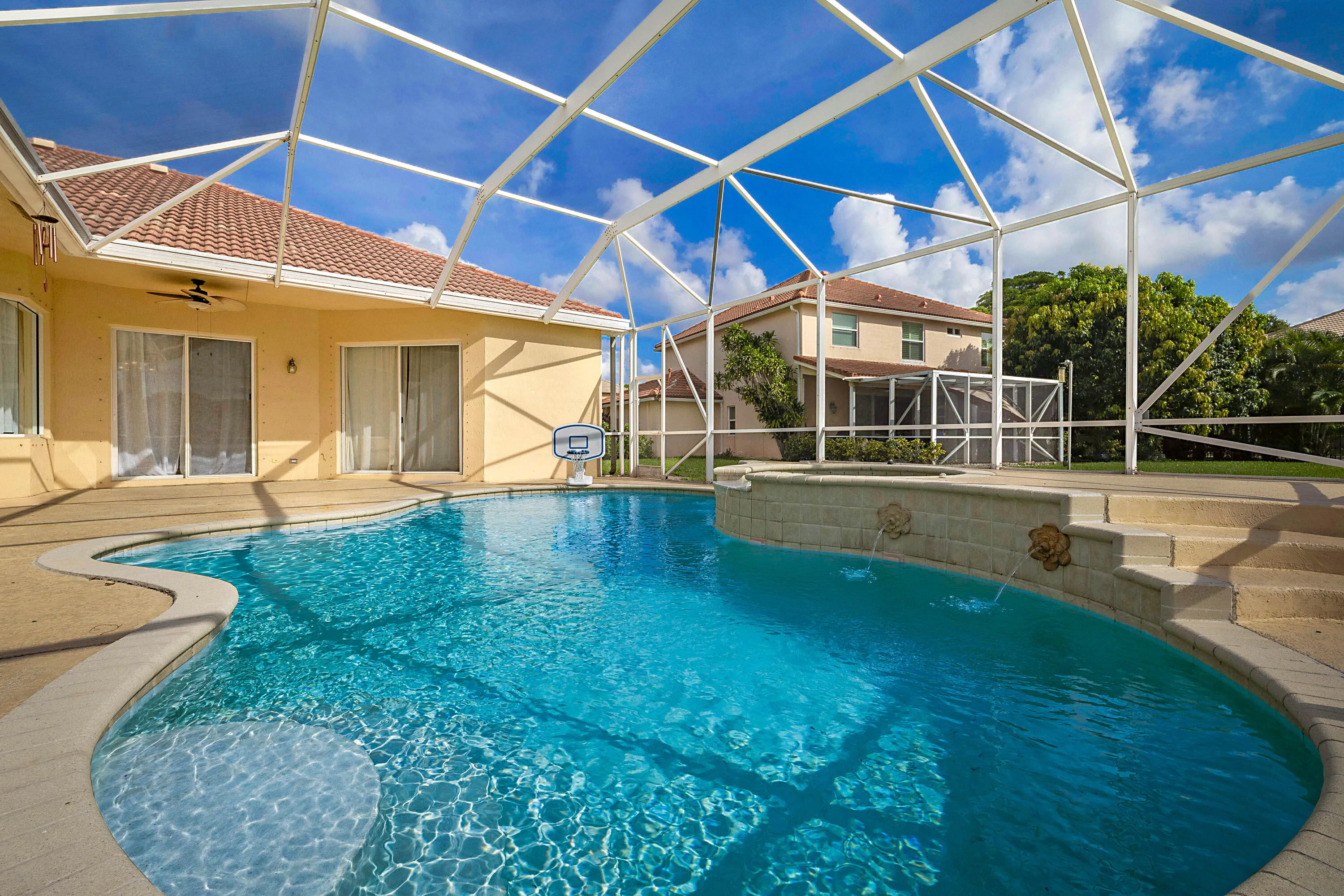 Screened-in outdoor living space featuring a freeform pool, integrated spa with water features, and an expansive paved patio