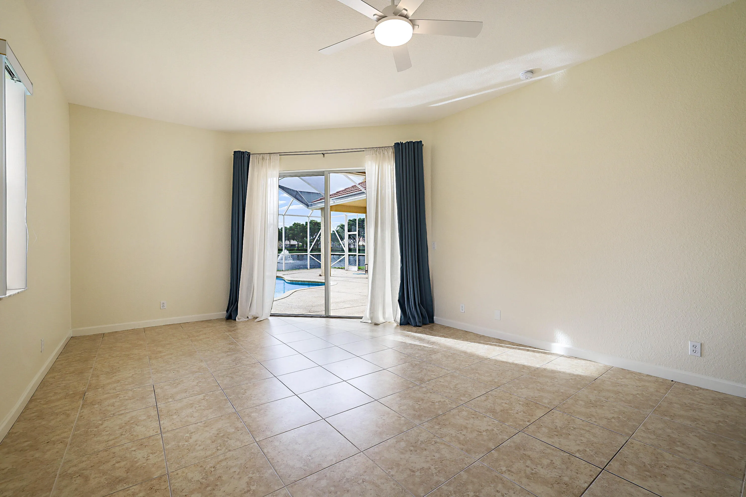 Spacious interior with tile flooring, ceiling fan with integrated lighting, and French doors opening to outdoor pool area