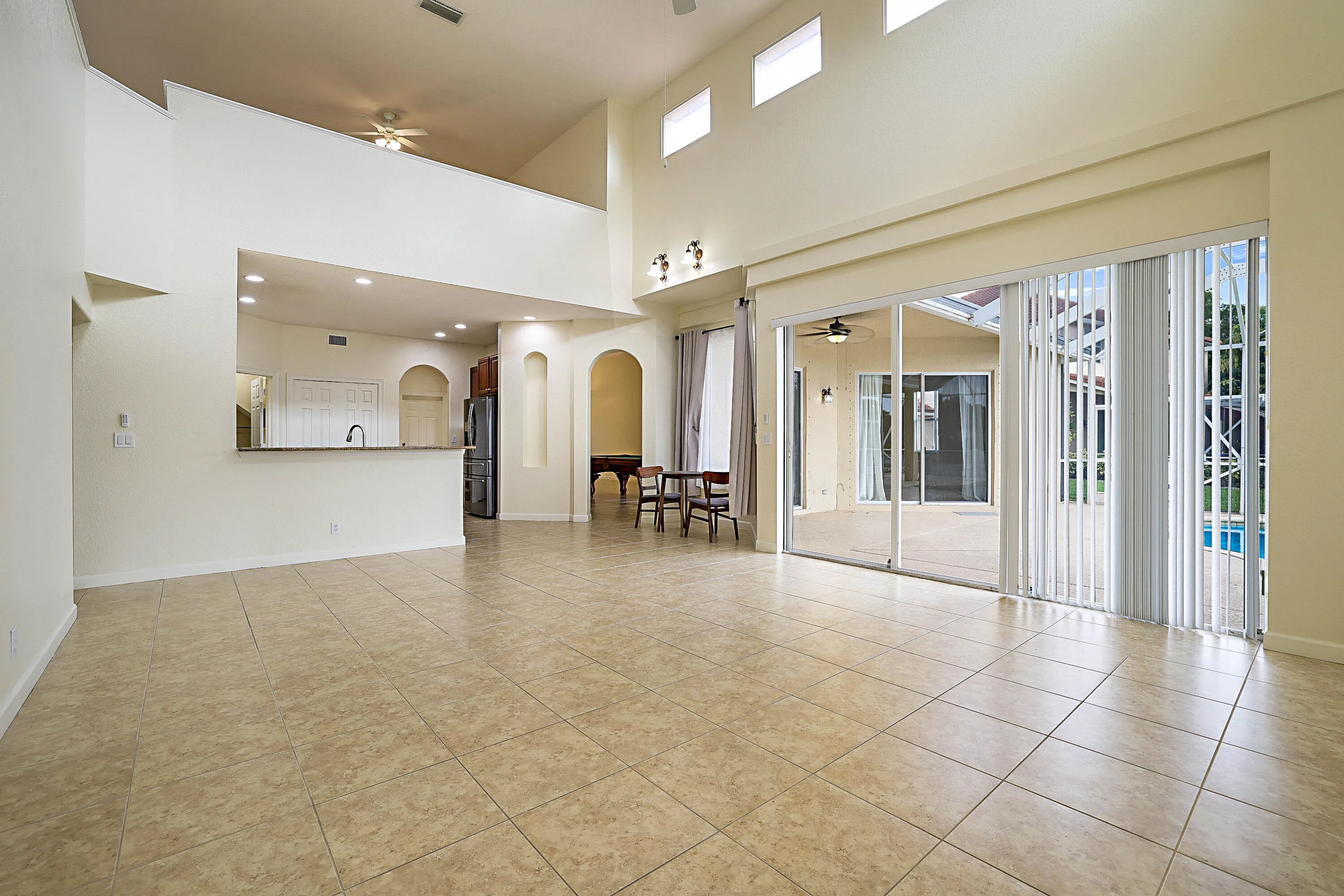 Expansive tiled flooring, high vaulted ceilings, and a kitchen pass-through with a breakfast bar