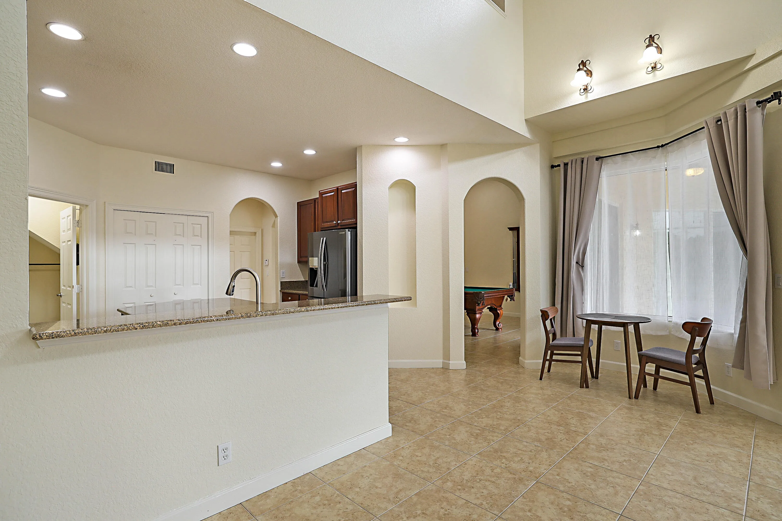 Open-concept living area featuring recessed lighting throughout, arched architectural alcoves, stainless steel appliances, and tile flooring