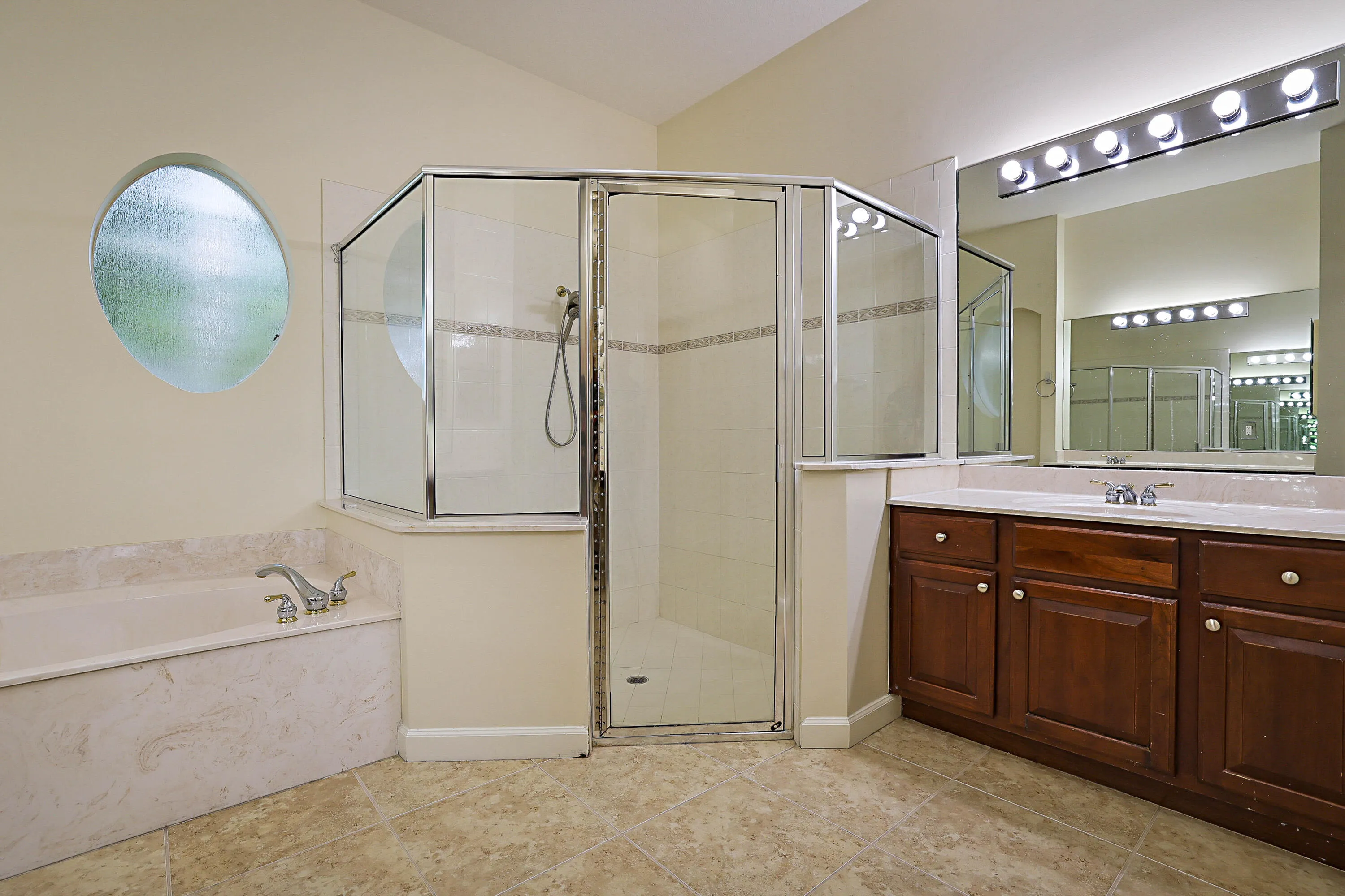 Spa-inspired master bathroom featuring a soaking tub with deck-mounted faucet, a frameless glass enclosed shower with multiple showerheads, wood-finish vanity cabinetry with dual sinks, polished countertops, and recessed and pendant lighting throughout