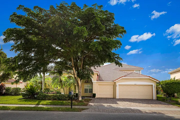 Two-story stucco exterior with a tiled roof, paver driveway, and an attached two-car garage