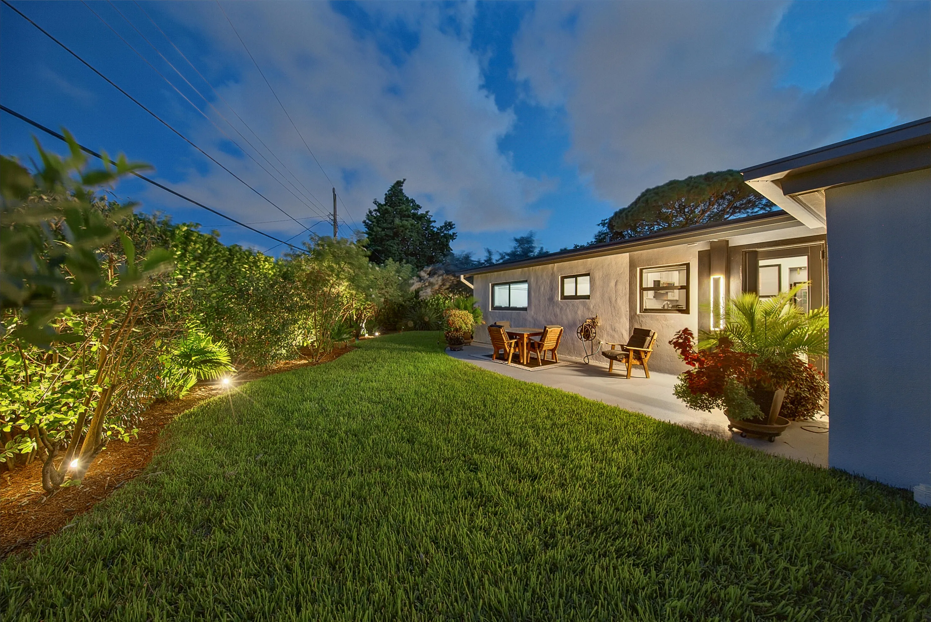 Manicured lawn with a concrete patio, exterior lighting, and mature landscaping