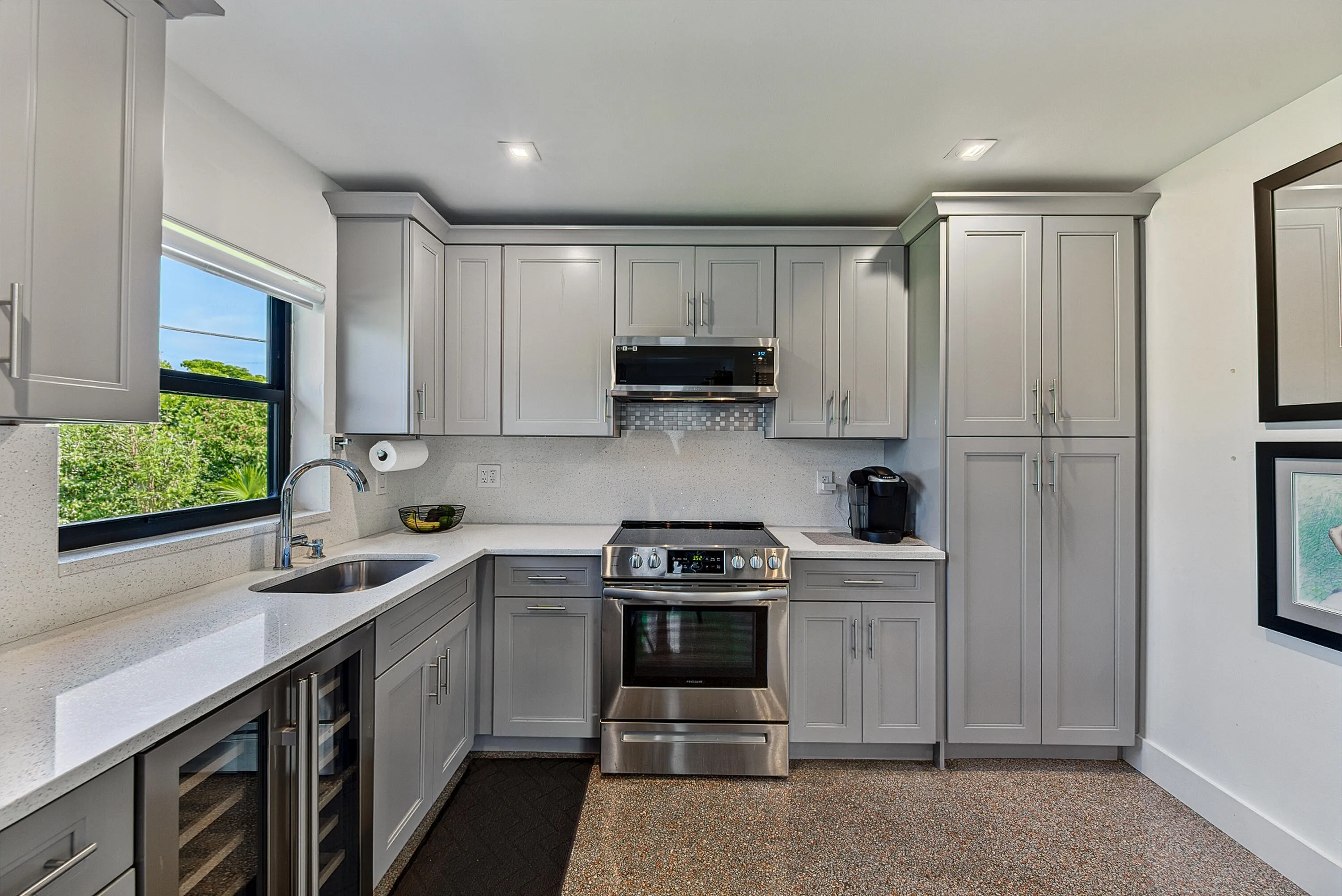 Thoughtfully designed kitchen with light gray cabinetry, stainless steel appliances, a built-in wine refrigerator, and quartz countertops.