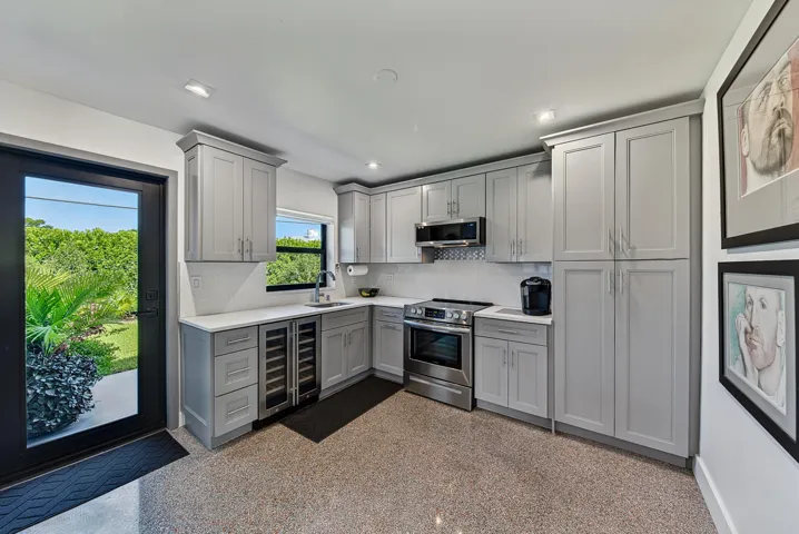 Thoughtfully designed kitchen with light gray cabinetry, stainless steel appliances, a built-in wine refrigerator, and quartz countertops.