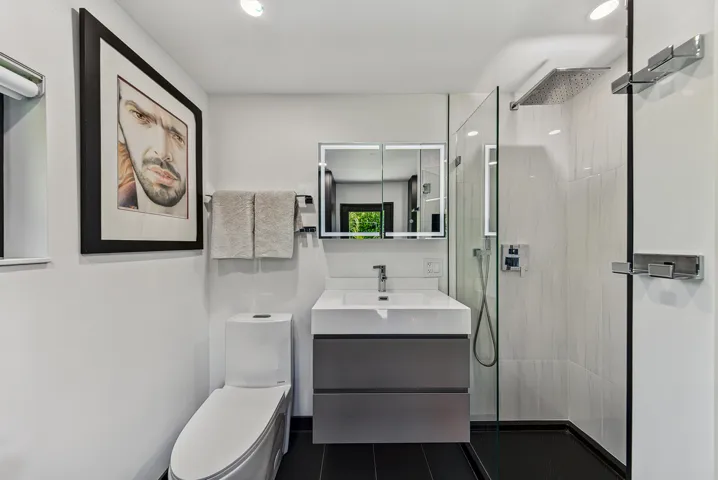 Second bath has a modern floating vanity with integrated sink, mirrored medicine cabinet with lighting, frameless glass shower enclosure, and a rainfall showerhead