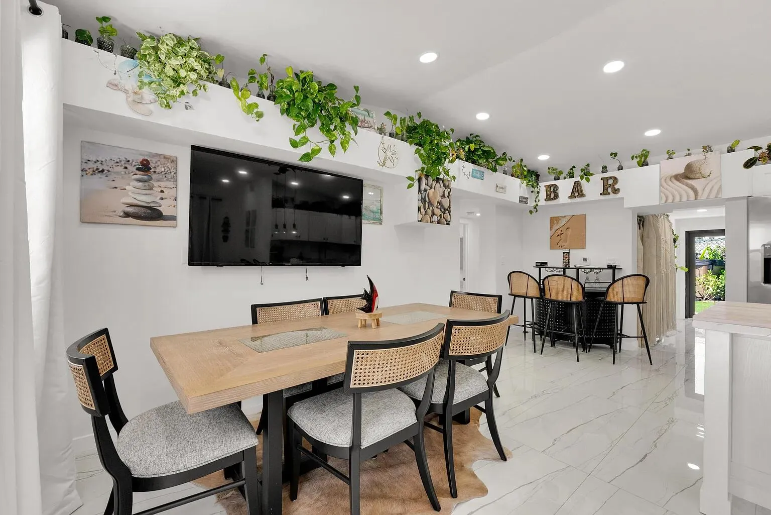 Recessed lighting illuminates the open-concept space featuring a built-in bar area, light-toned flooring, and a wall-mounted entertainment display