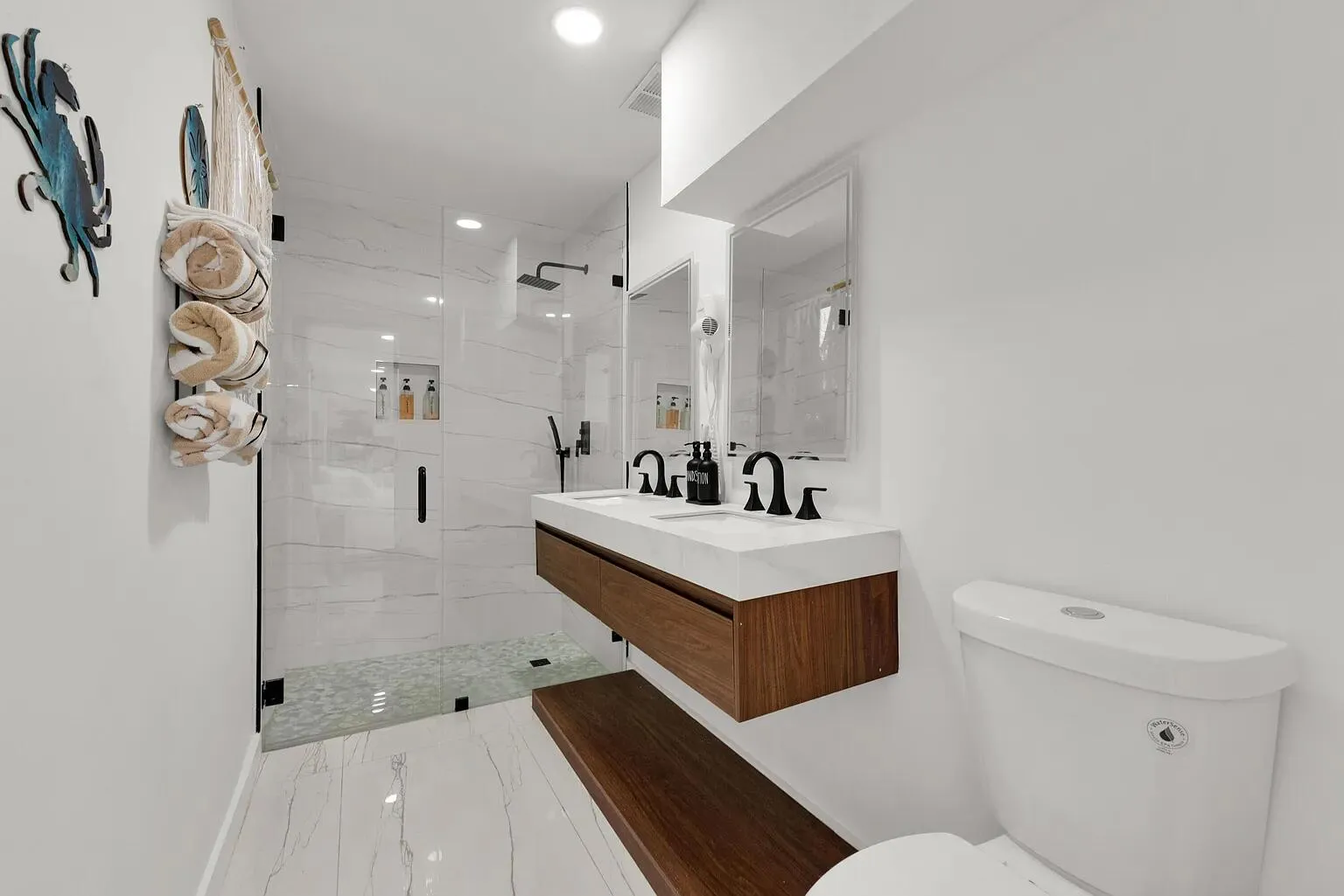 Walk-in shower with clear glass enclosure, a floating wood-finish vanity with dual sinks, and matte black fixtures