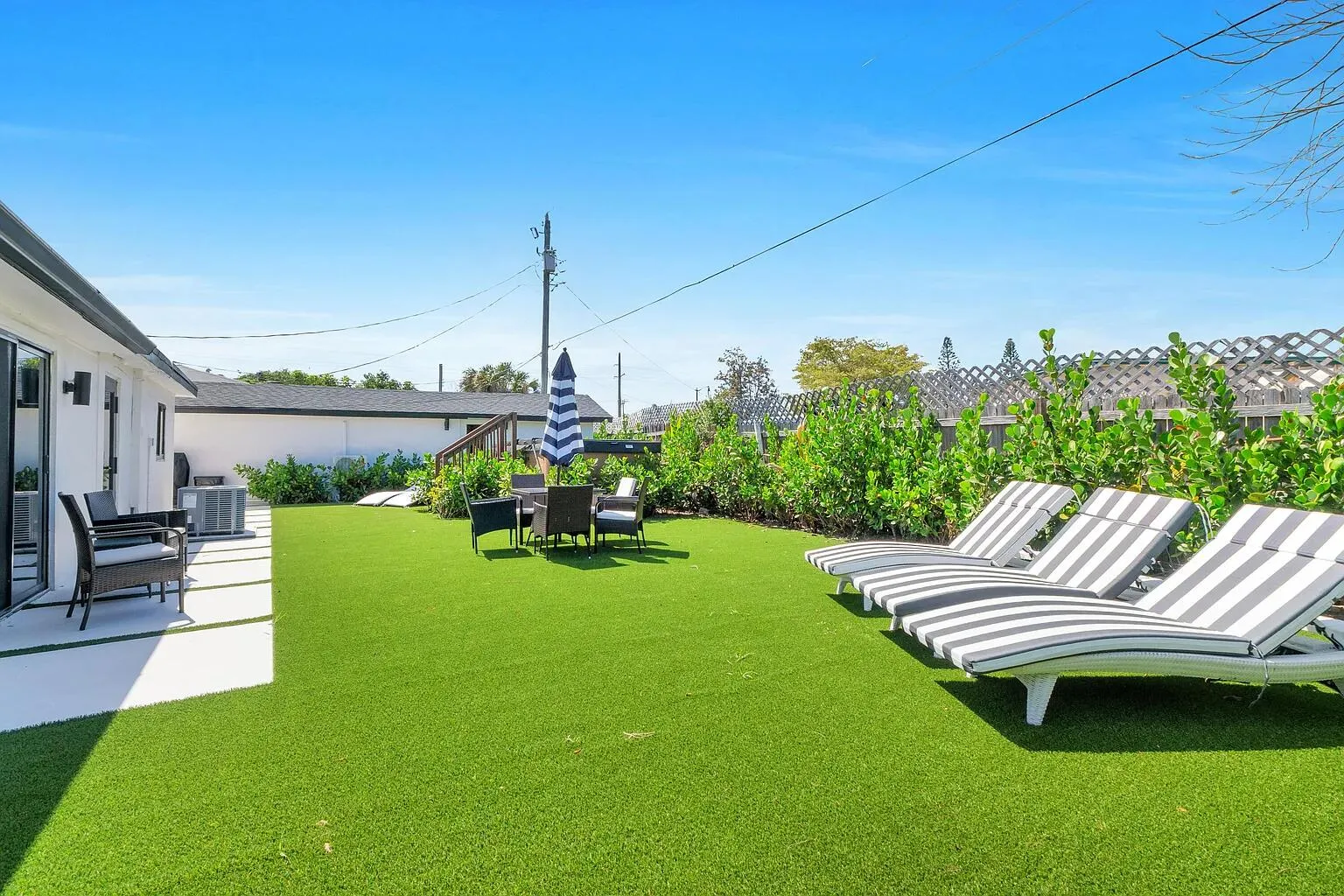Expansive backyard featuring artificial turf, a white paver patio, and mature perimeter landscaping
