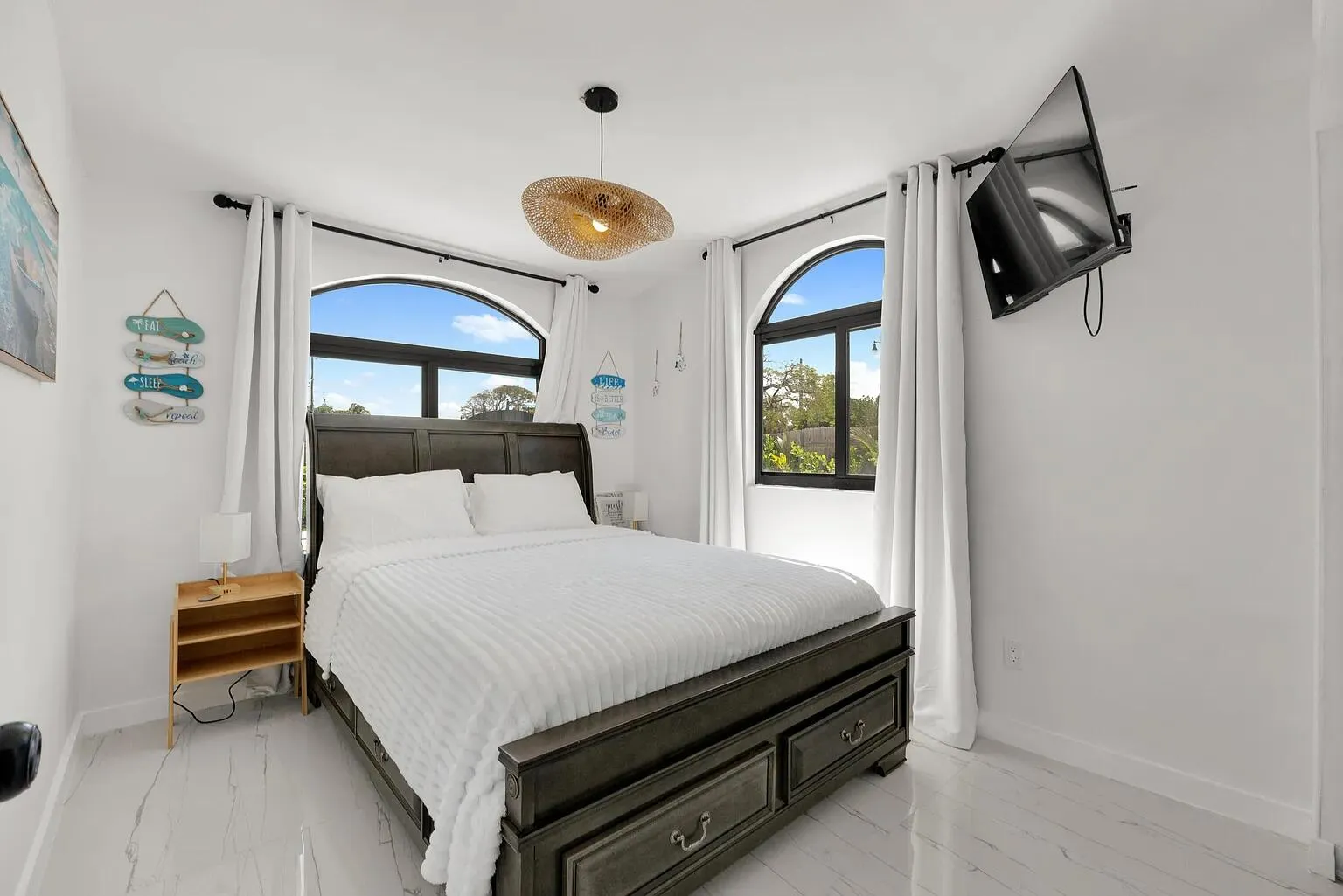Arched windows with black framing, white walls, wood-finish flooring, and a decorative ceiling light fixture