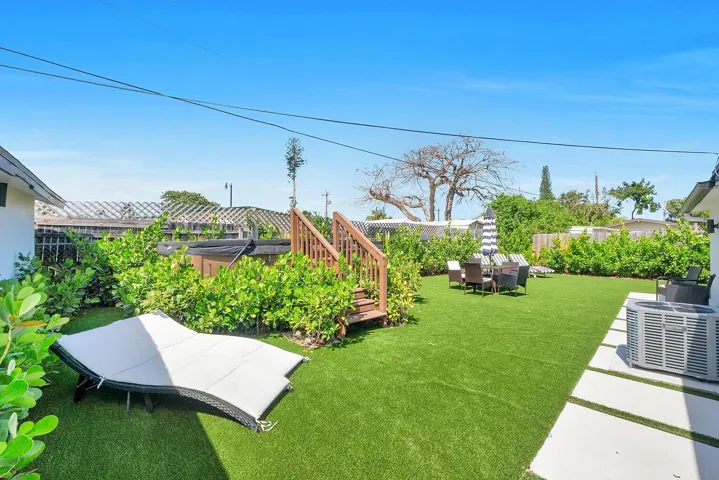 Manicured artificial turf lawn, raised wooden deck, built-in spa, concrete paver pathway, and perimeter landscaping