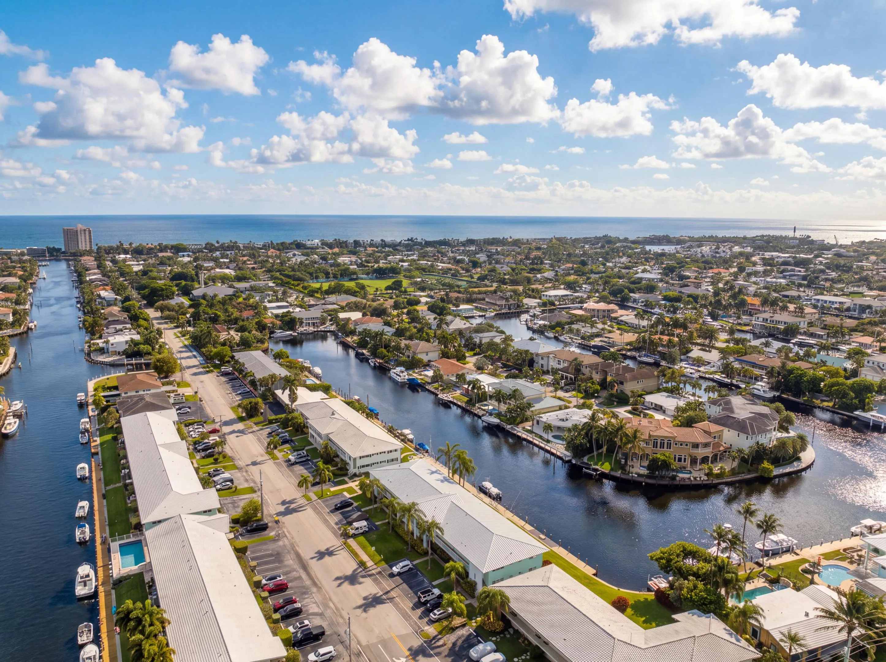 Waterfront community featuring multiple canals with boat access, residential properties with private docks, a distant ocean horizon, and abundant mature trees