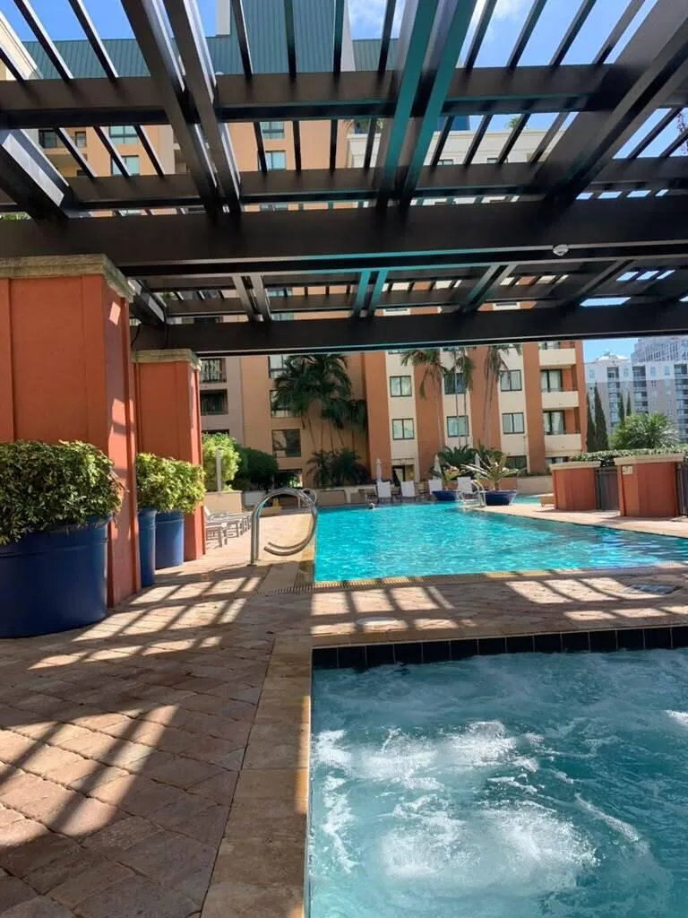 Resort-style pool with integrated spa, paver patio, architectural pergola, and mature landscaping