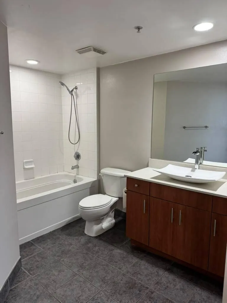Bathroom featuring a white subway tile tub surround, white bathtub, dark tile flooring, wood-finish vanity with ample storage, and a vessel sink