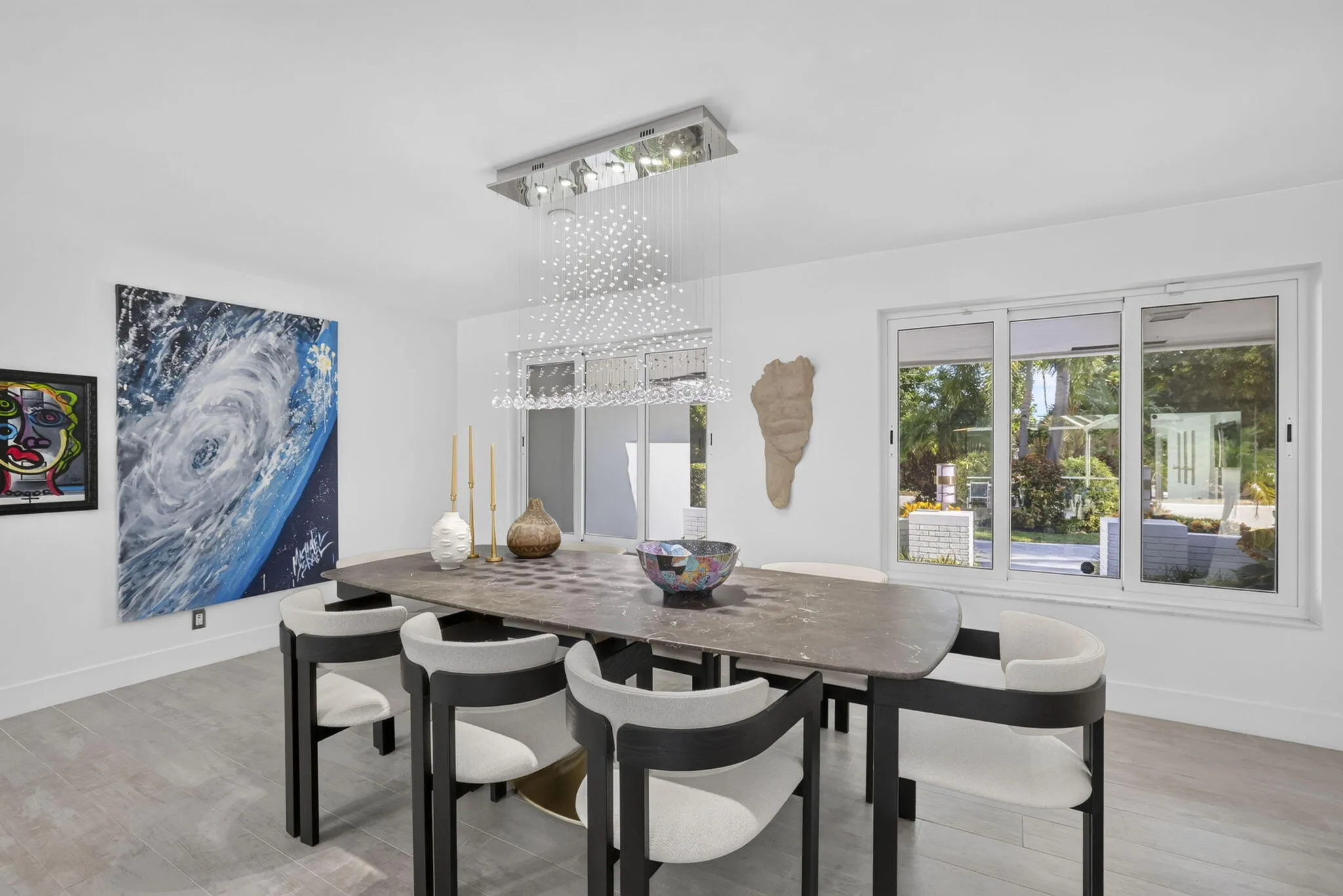 Expansive windows providing natural light, sleek tile flooring, and a contemporary linear chandelier with crystal accents
