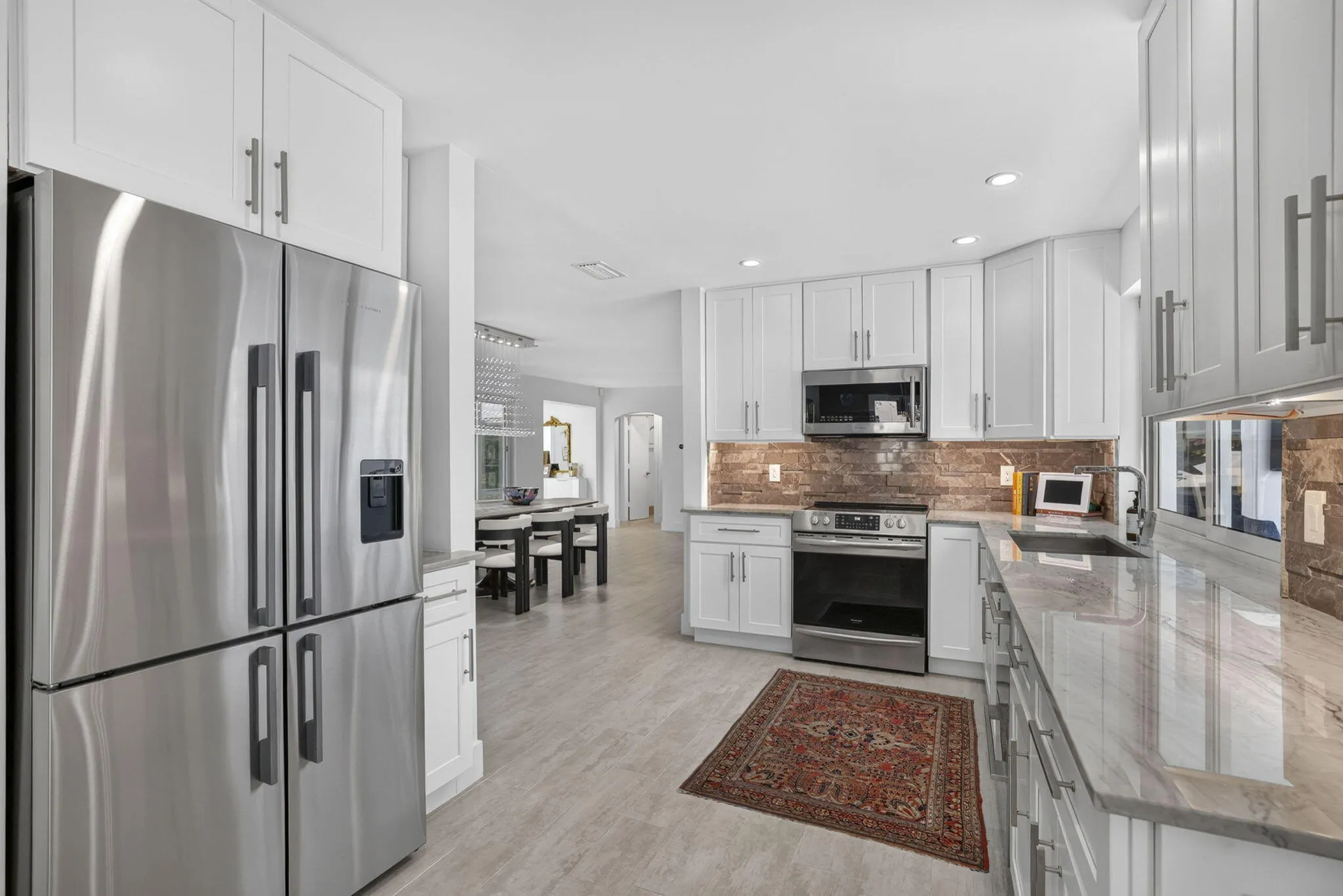 Stainless steel French door refrigerator, white shaker-style cabinetry, stainless steel appliances, stone backsplash, and light-toned countertop