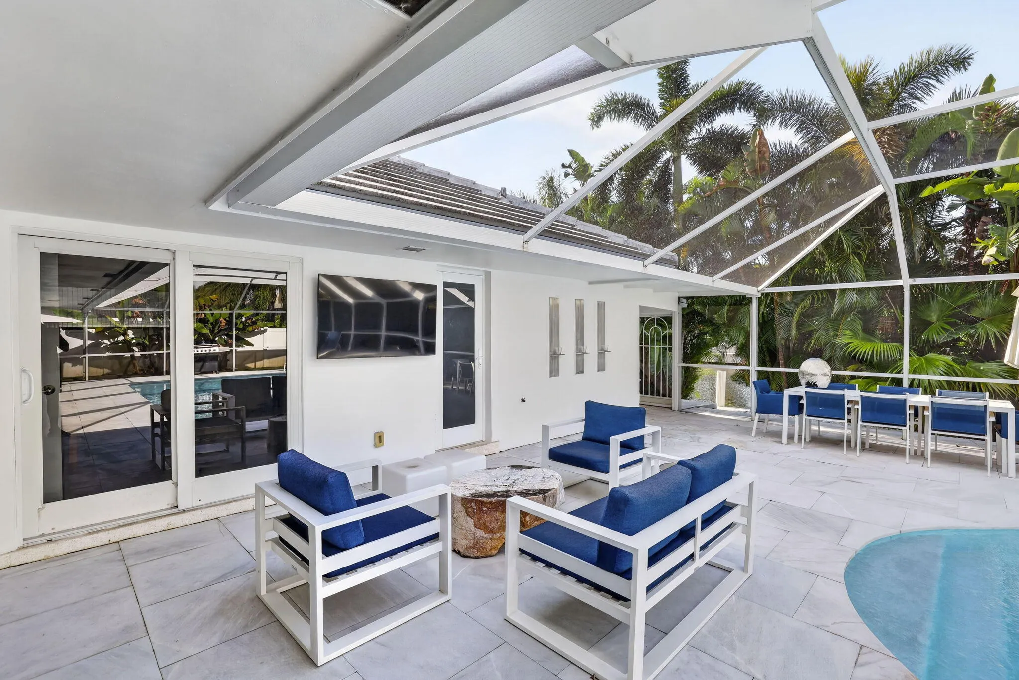 Screened outdoor living area with a stone tile patio, built-in pool, and tropical landscaping