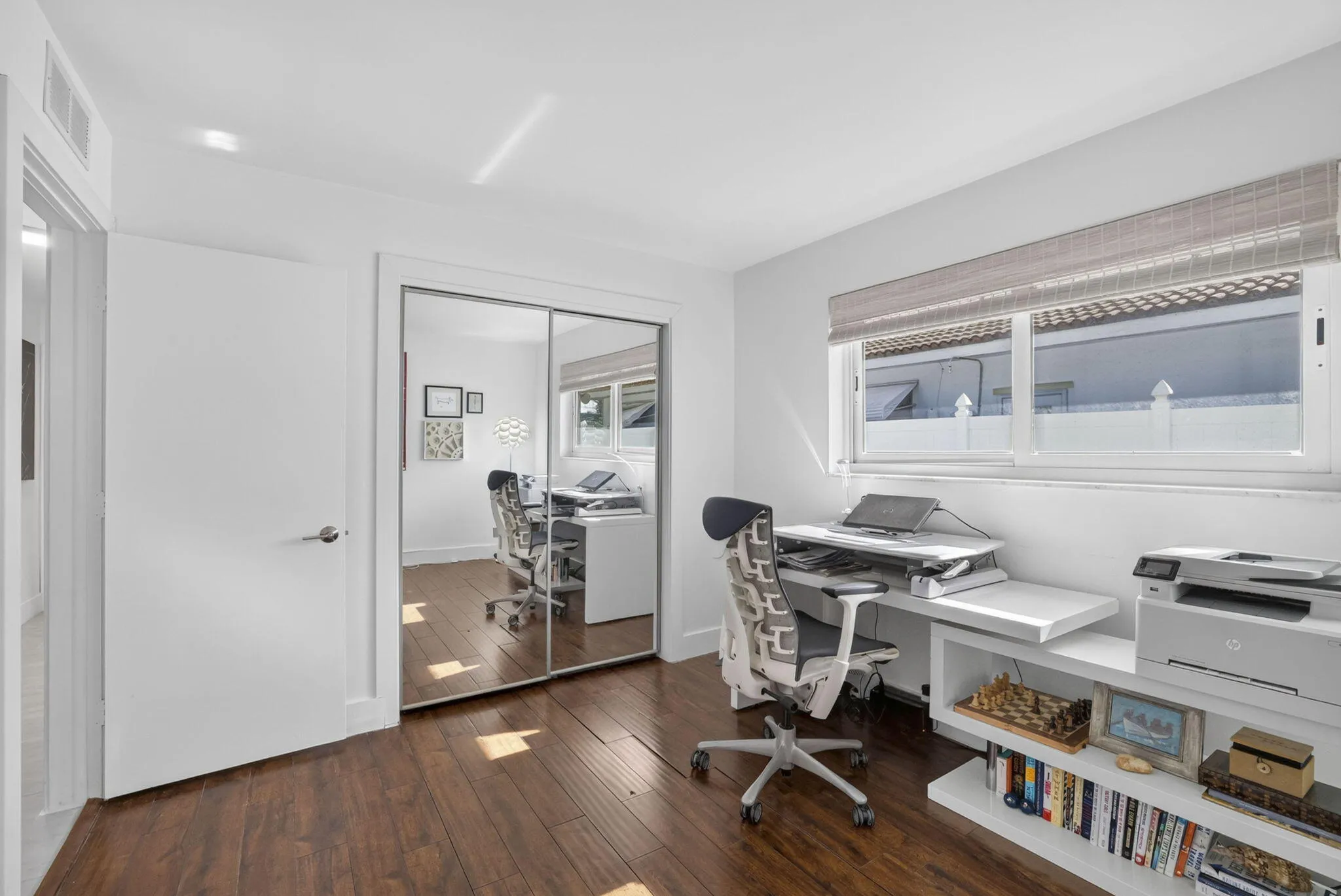 Wood-finish flooring, white walls, mirrored closet doors, and white window blinds