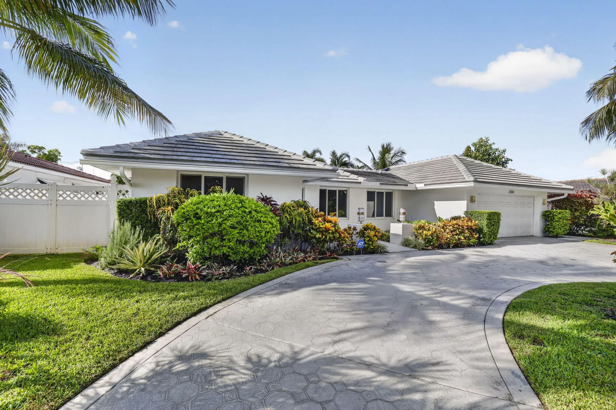 Single-story residence featuring a gray tile roof, attached garage, curved concrete driveway, and established landscape planting