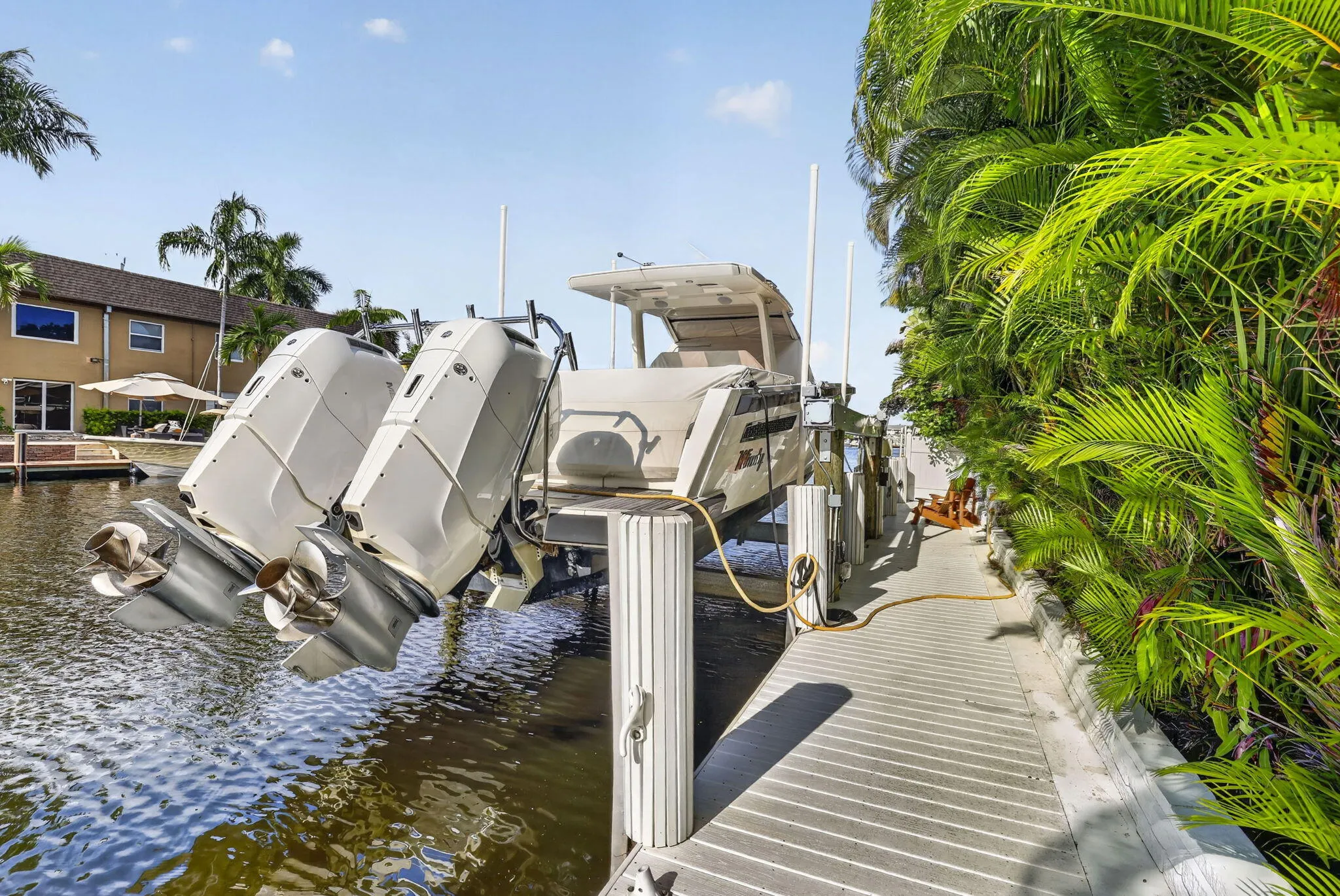 Waterfront property featuring a private boat lift, a boat on a lift, a wooden dock, and lush tropical landscaping