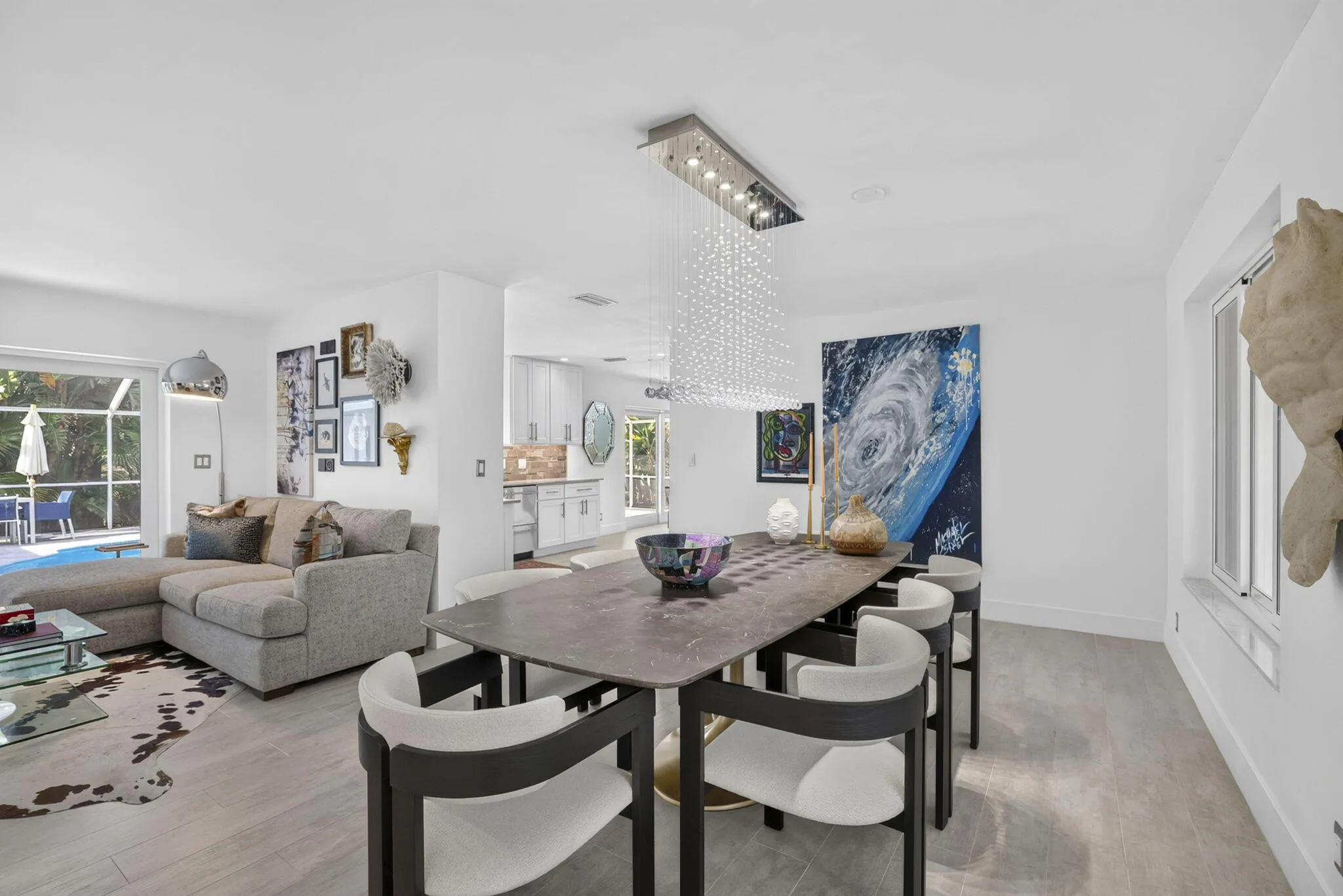 Open-concept living and dining area, a contemporary linear crystal chandelier, and a sliding glass door leading to an outdoor space
