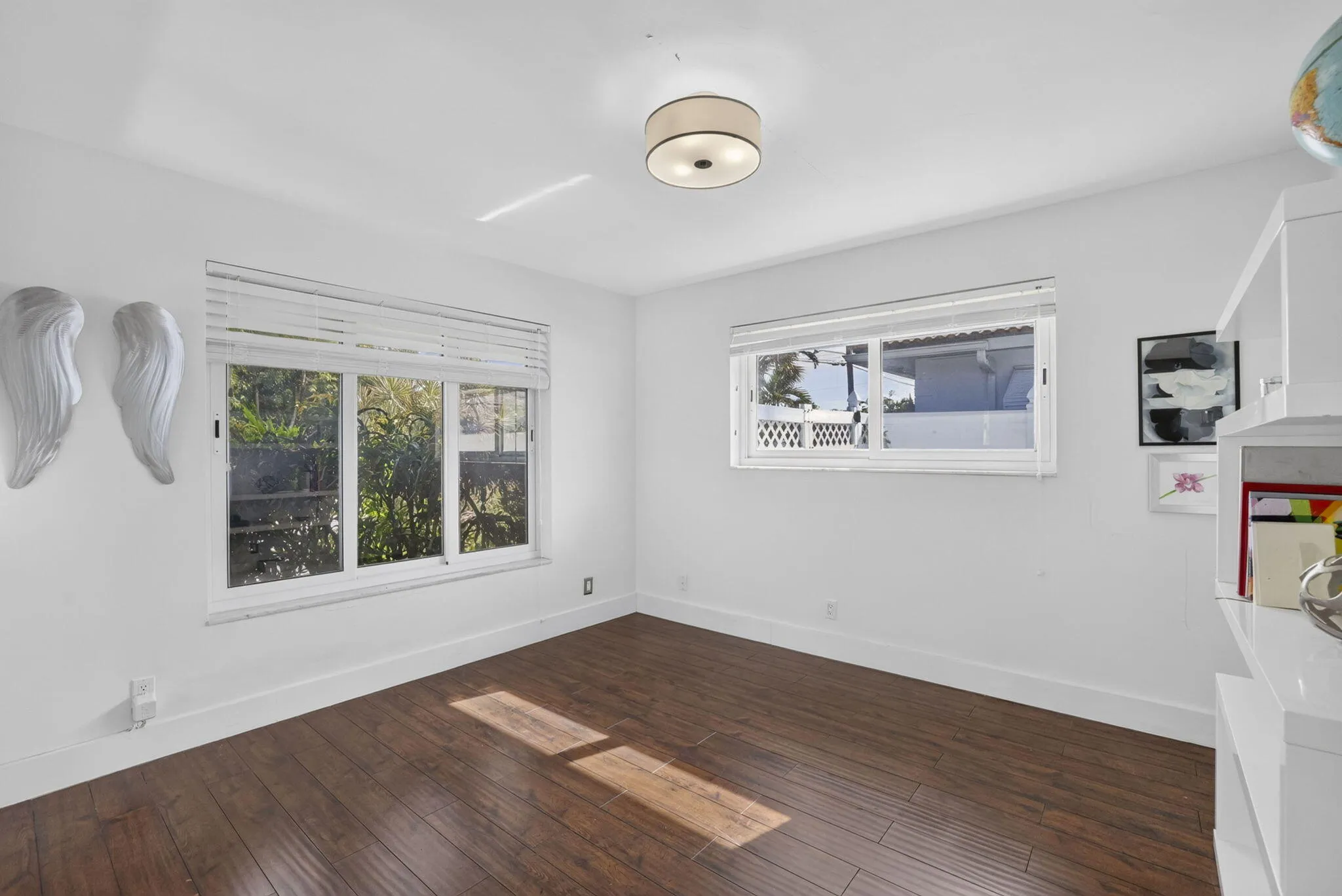 Spacious room featuring rich wood-finish flooring, white walls, and a contemporary ceiling fixture