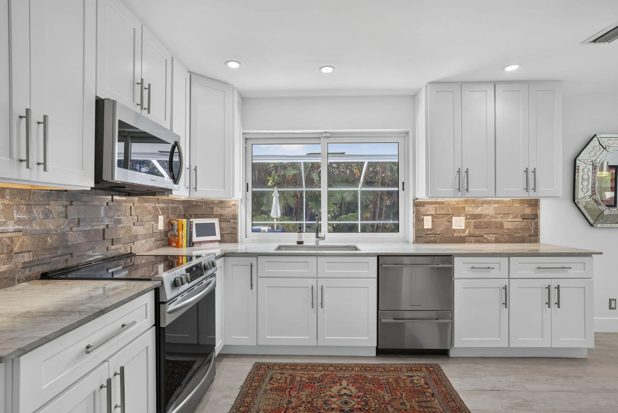 White shaker-style cabinetry, stainless steel appliances, stacked stone backsplash, light-toned countertops, and recessed lighting