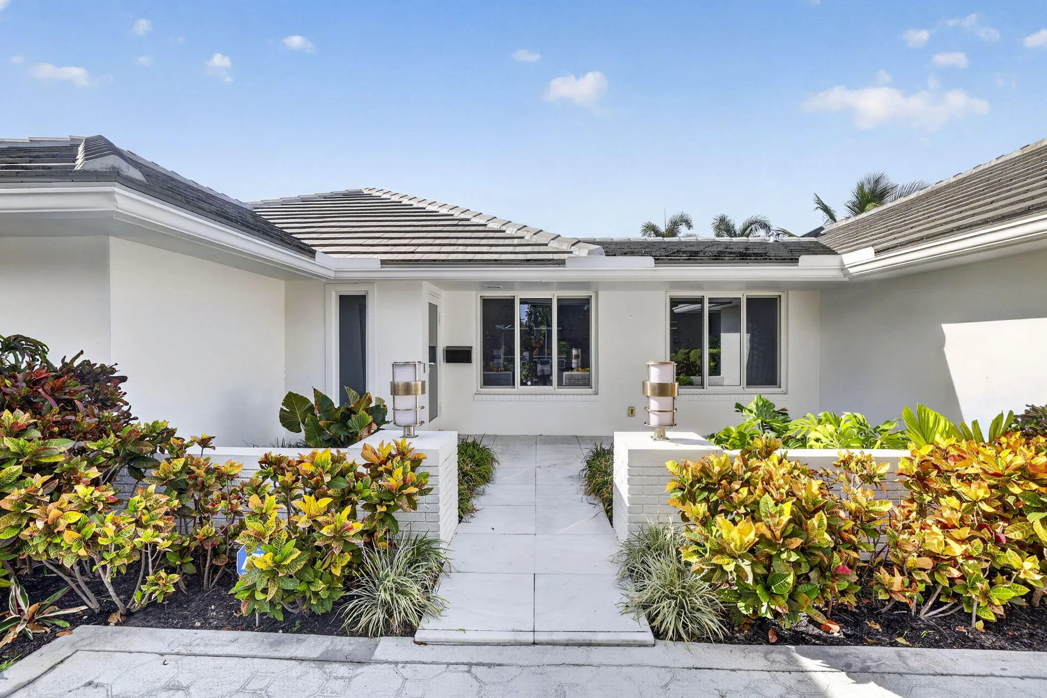 Smooth stucco exterior with a tiled roof, featuring a white brick planter and a paver walkway