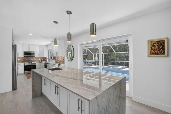 Kitchen island with integrated sink, stainless steel appliances, white cabinetry, and sliding glass doors opening to an outdoor pool area with a screened enclosure