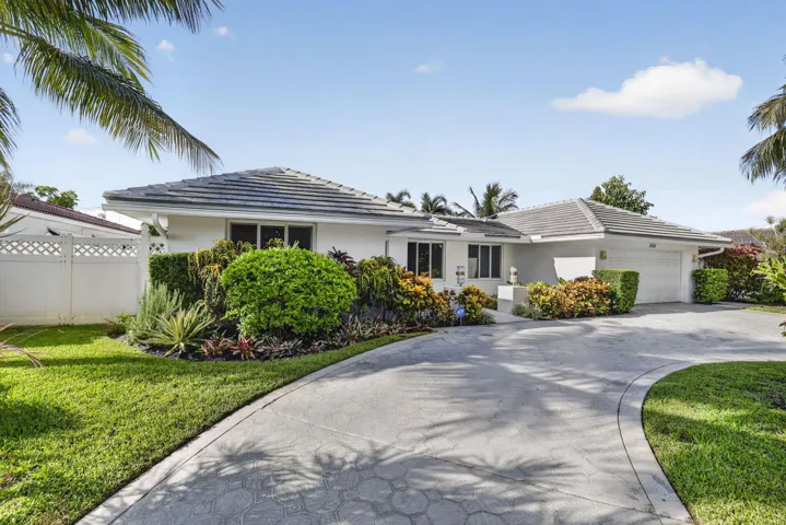 Single-story residence featuring a gray tile roof, attached garage, curved concrete driveway, and established landscape planting