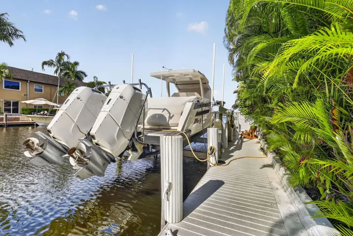 Waterfront property featuring a private boat lift, a boat on a lift, a wooden dock, and lush tropical landscaping