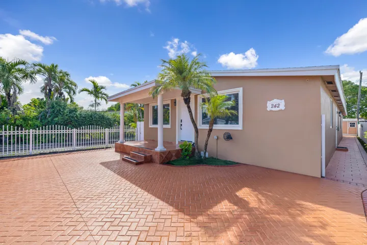 A welcoming front porch, tropical palms, and a broad paved frontage introduce this Hialeah home.