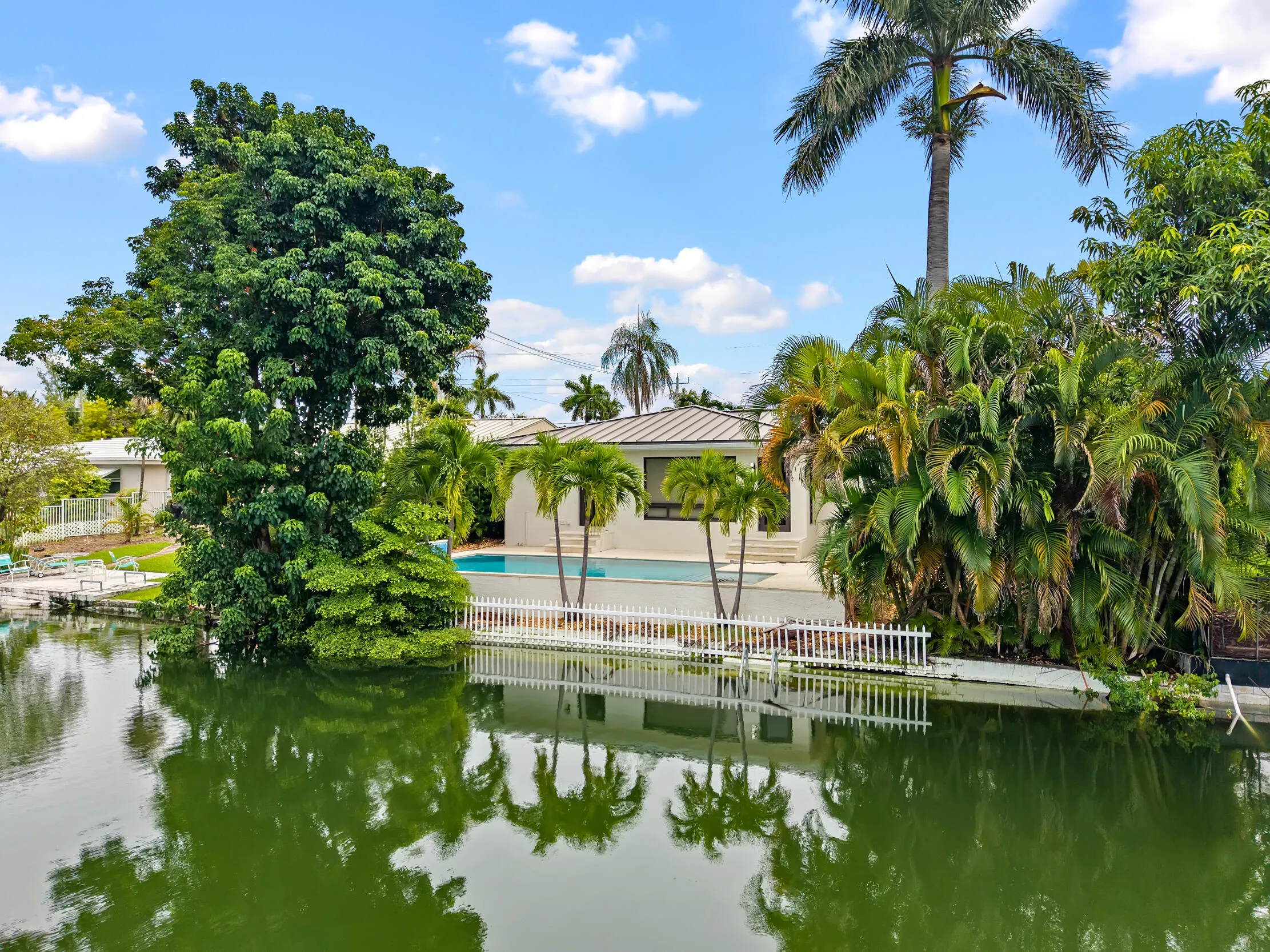Canal-front property featuring a white exterior, private swimming pool, and established tropical landscaping