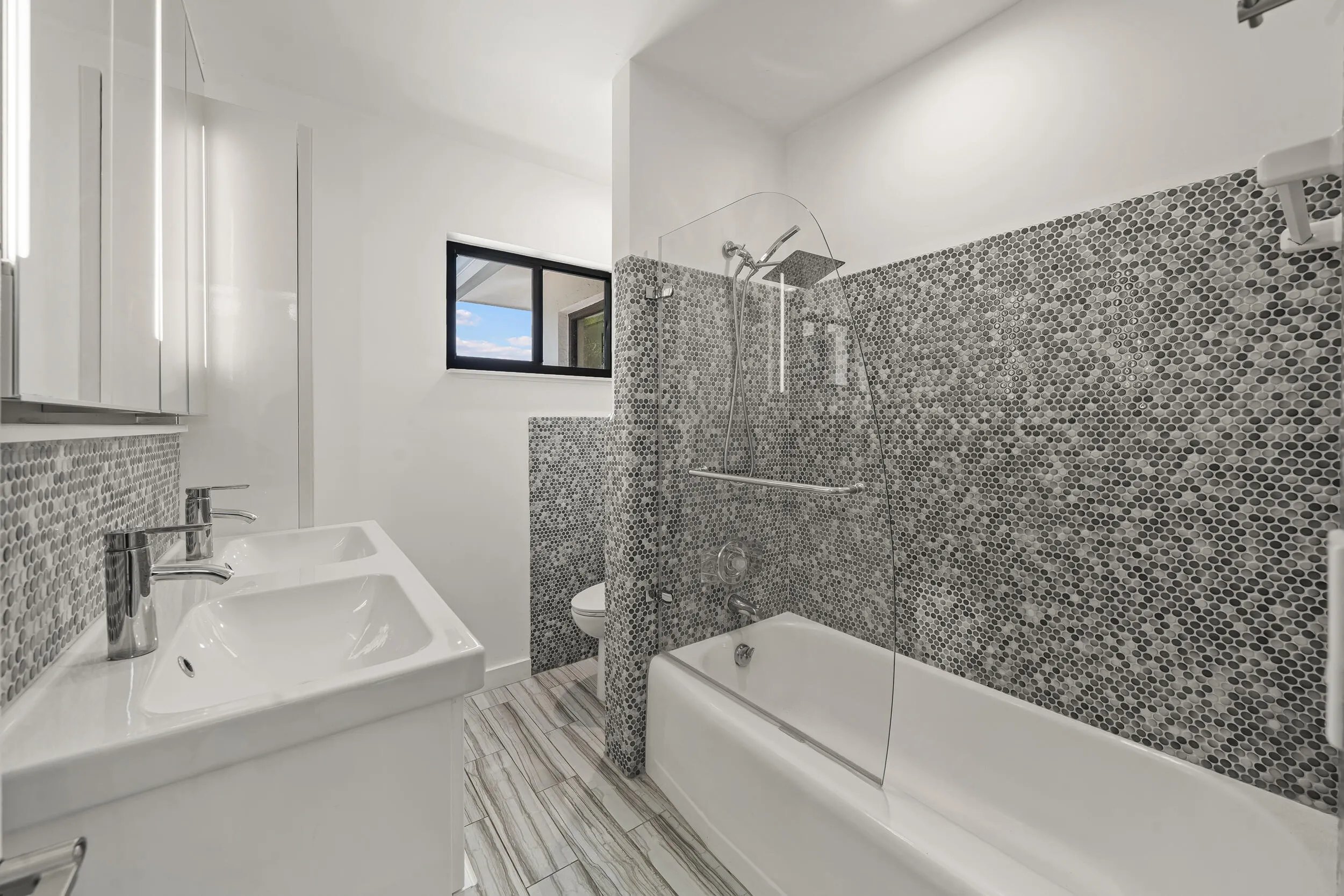 Dual vanity with integrated sinks, mosaic tile backsplash, wood-finish flooring, full-size bathtub, and glass shower partition