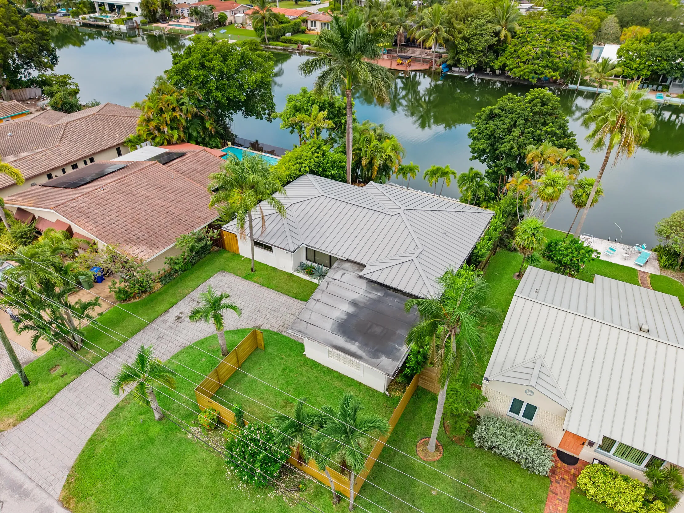 Waterfront property featuring a metal roof, mature landscaping, and a paver driveway
