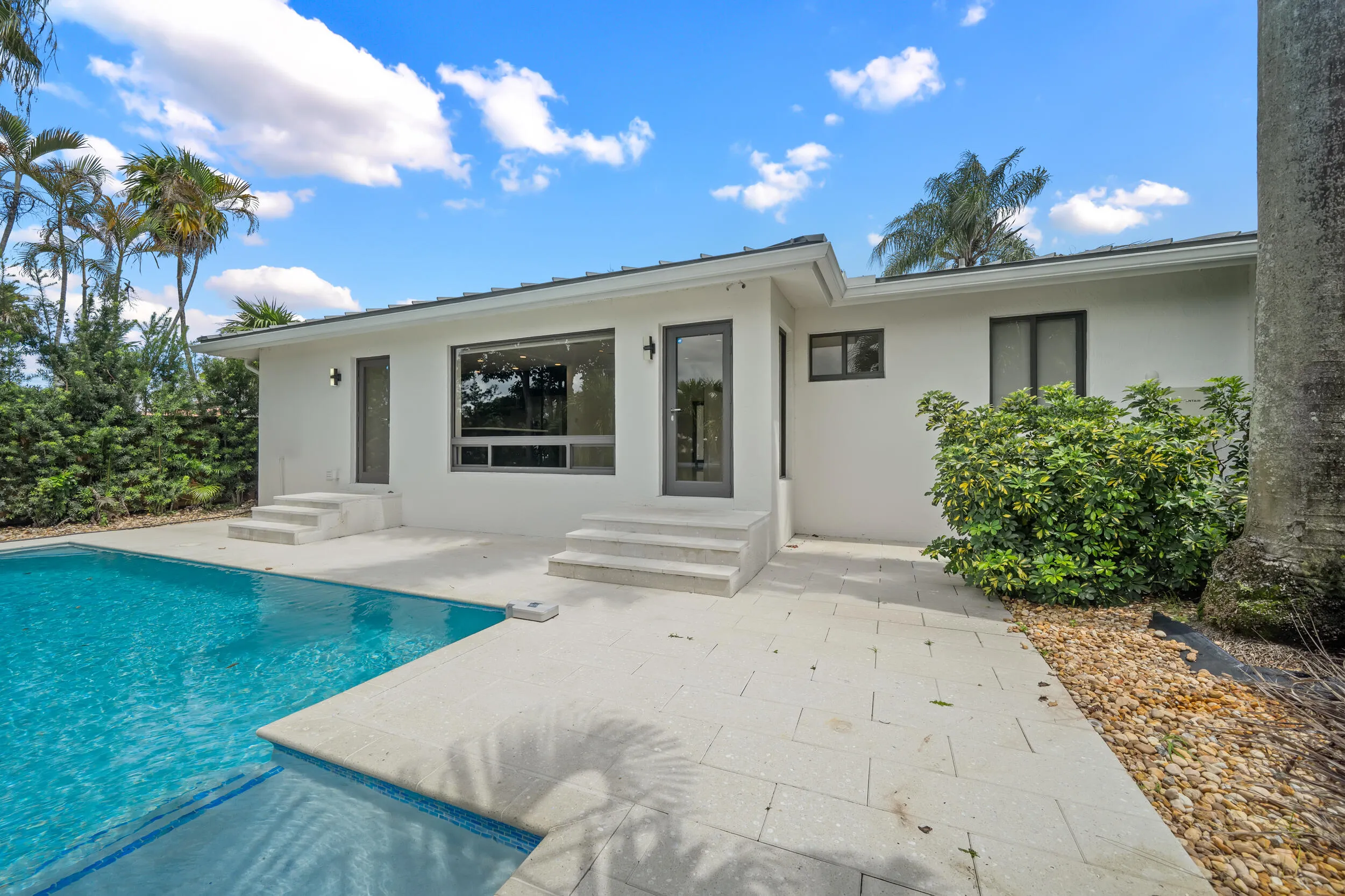 Exterior featuring a swimming pool with integrated spa, white stucco finish, large dark-framed windows, and a paved patio area