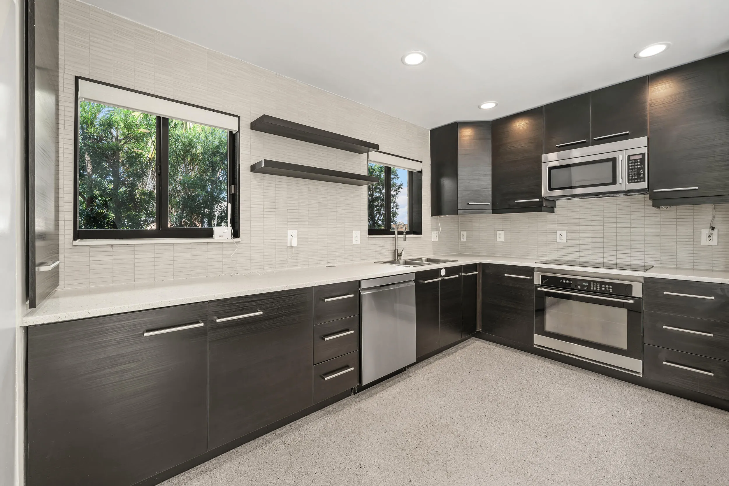 Kitchen featuring dark wood-finish cabinetry, stainless steel appliances, light-toned countertops, and a full-height tile backsplash