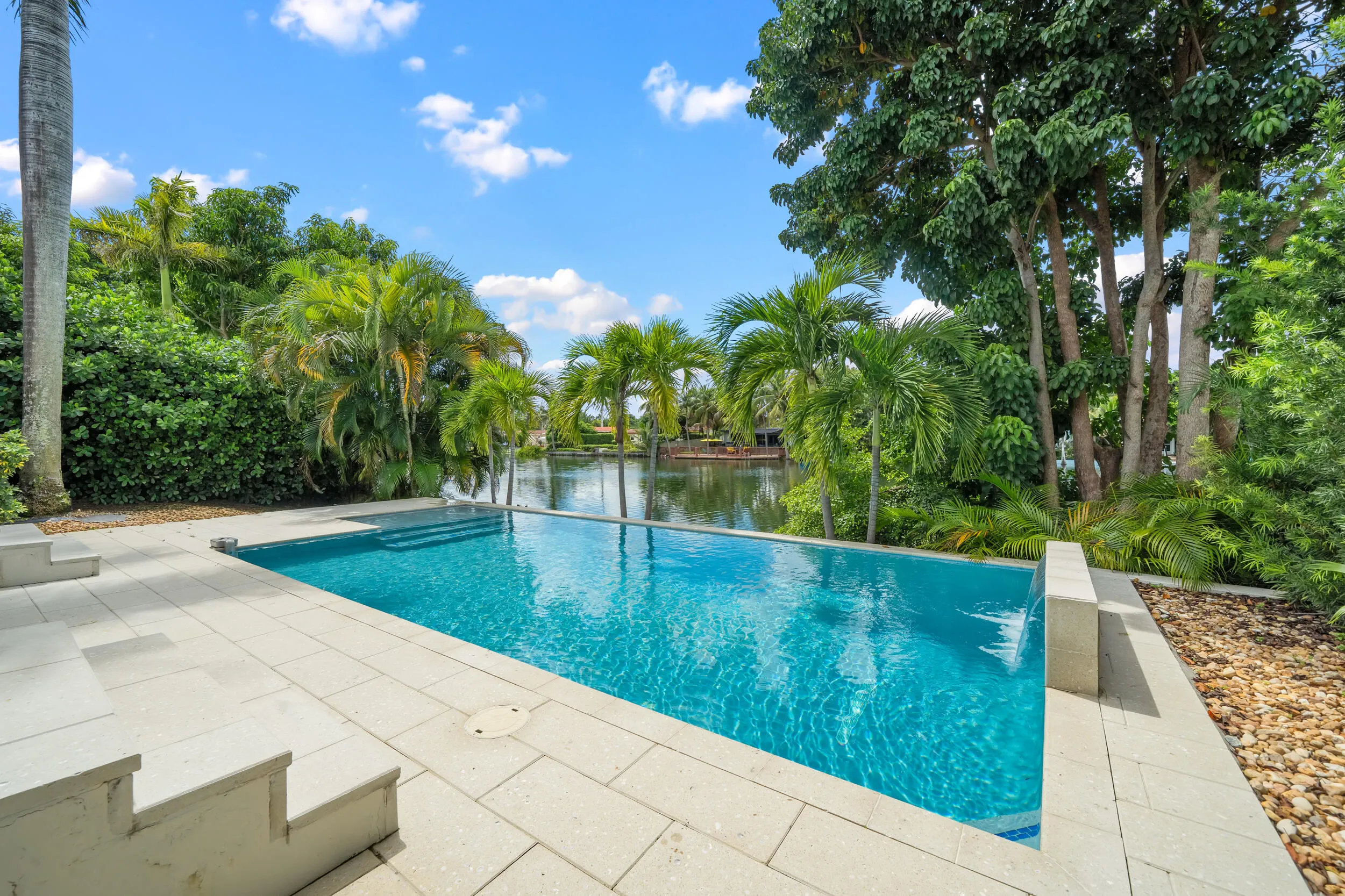 Infinity-edge pool with integrated steps, surrounded by a stone paver patio