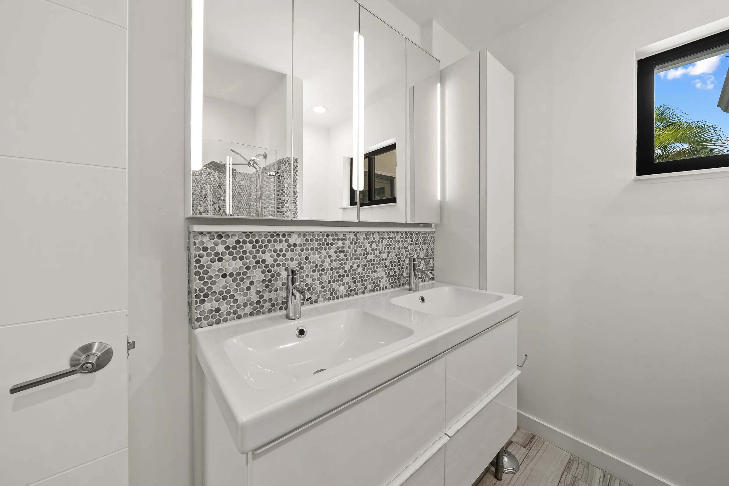 Dual vanity with integrated sinks, mosaic tile backsplash, illuminated medicine cabinets, and wood-finish flooring