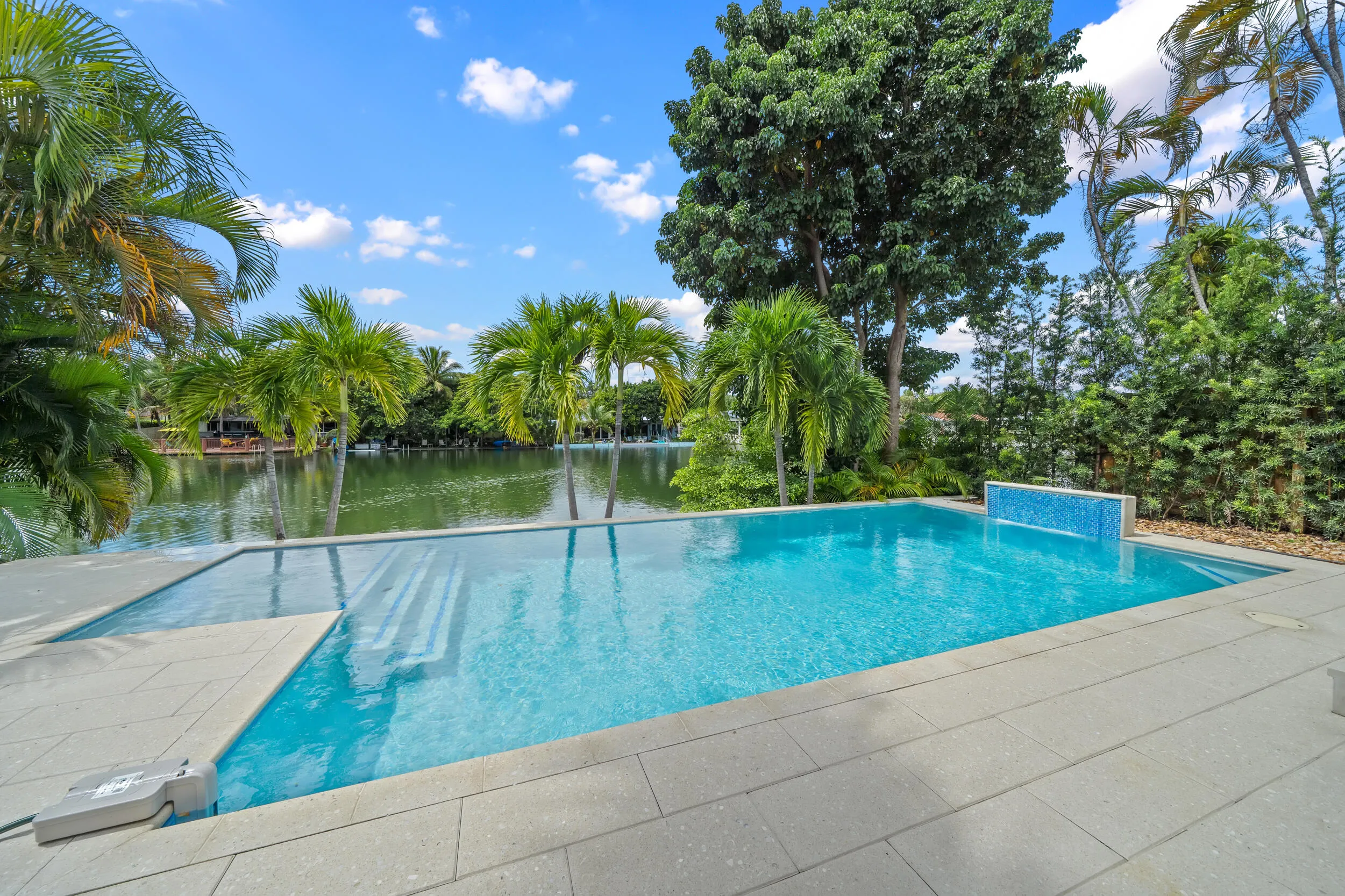 Expansive swimming pool with integrated steps, a decorative water feature with blue tile, and surrounding stone-finish decking