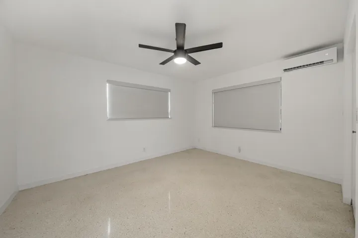 Bright interior with two windows, a ceiling fan, and a wall-mounted air conditioning unit