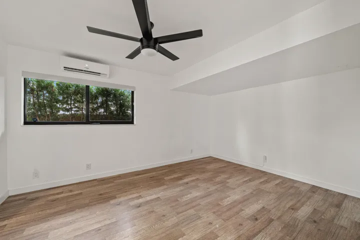 White walls, wood-finish flooring, modern ceiling fan, window with exterior scenery, wall-mounted air conditioning unit