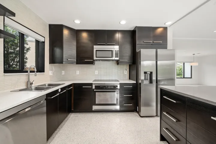 Modern kitchen featuring dark wood-finish cabinetry, light-toned countertops, stainless steel appliances, and a tiled backsplash